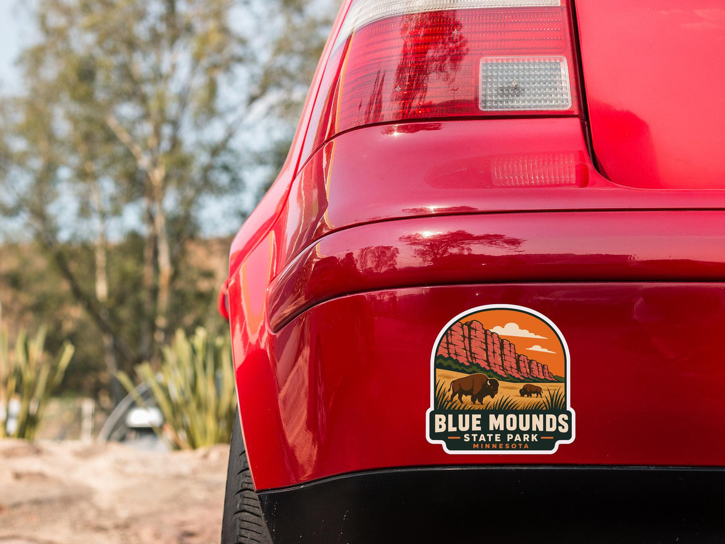 the rear end of a red car with a sticker on the trunk that says "BLUE MOUNDS STATE PARK MINNESOTA".