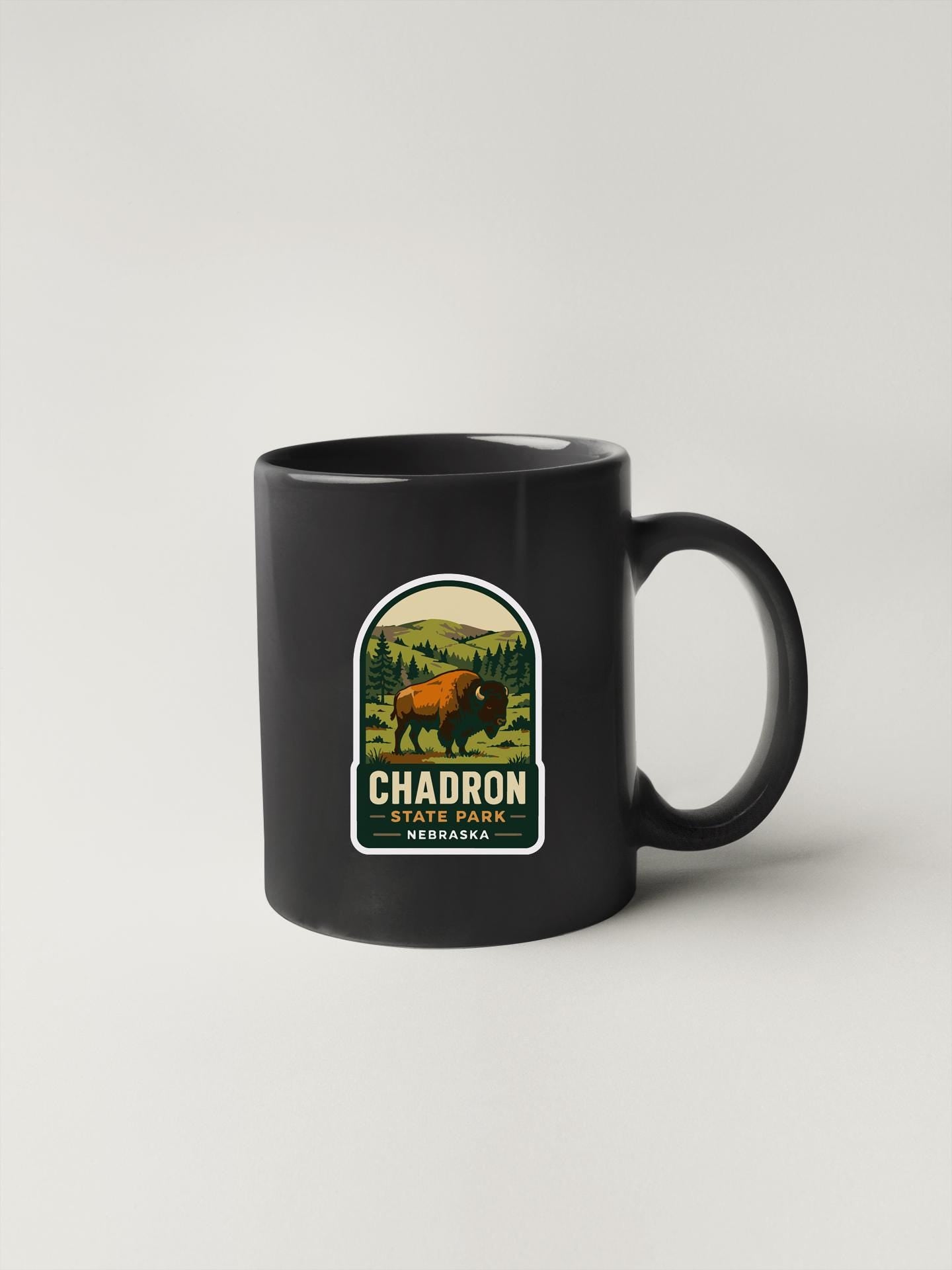 A black coffee mug with a graphic design featuring a bison in a natural setting, along with the text "CHADRON STATE PARK NEBRASKA".