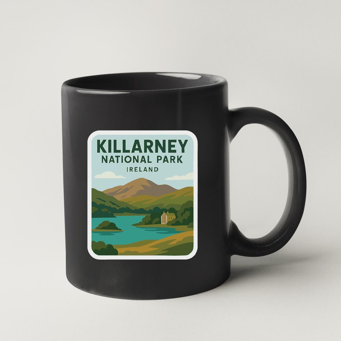 A black coffee mug with a sticker depicting a scenic landscape of Killarney National Park, Ireland.