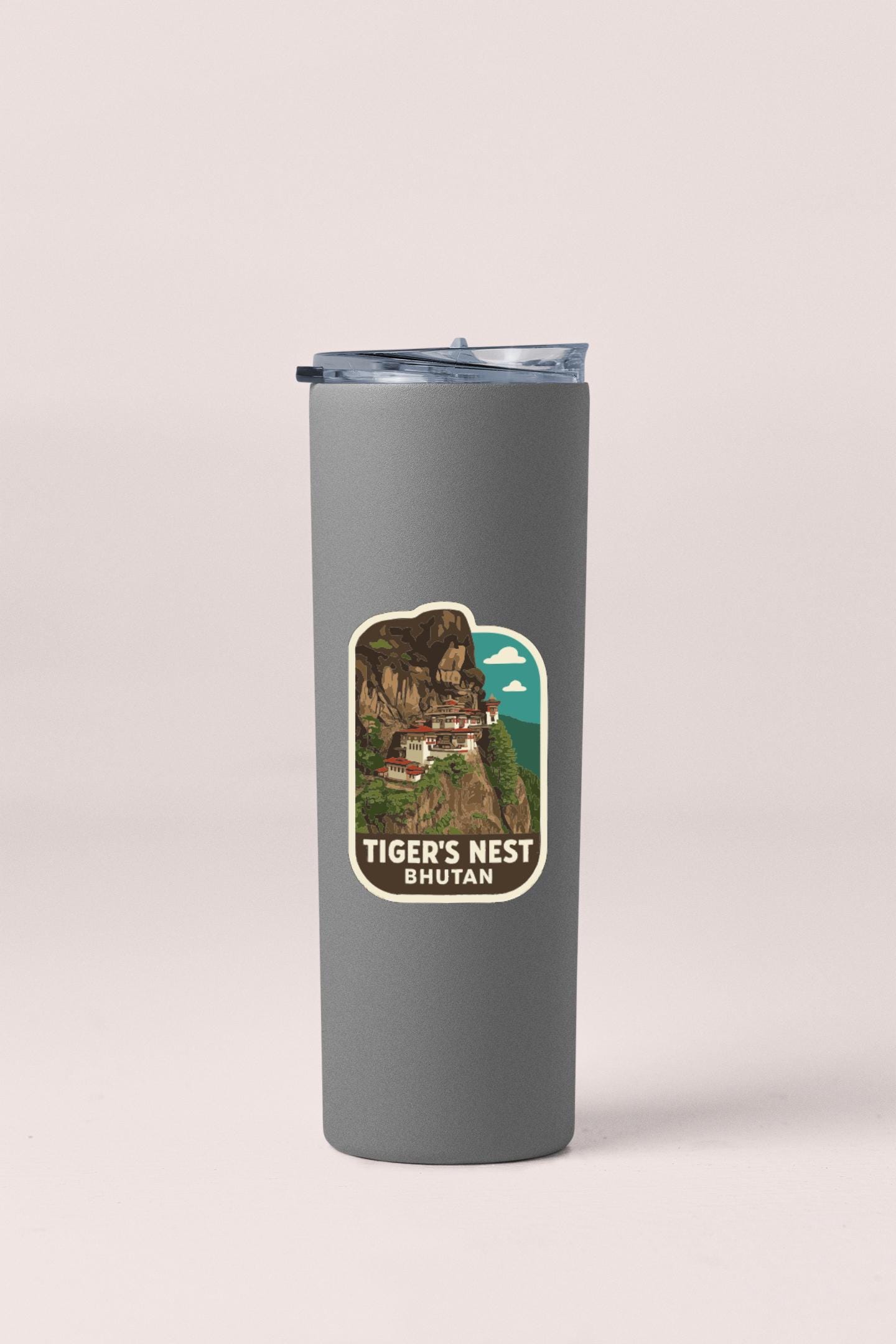 A gray tumbler with a sticker depicting a scenic mountain landscape and the text "TIGER'S NEST BHUTAN".