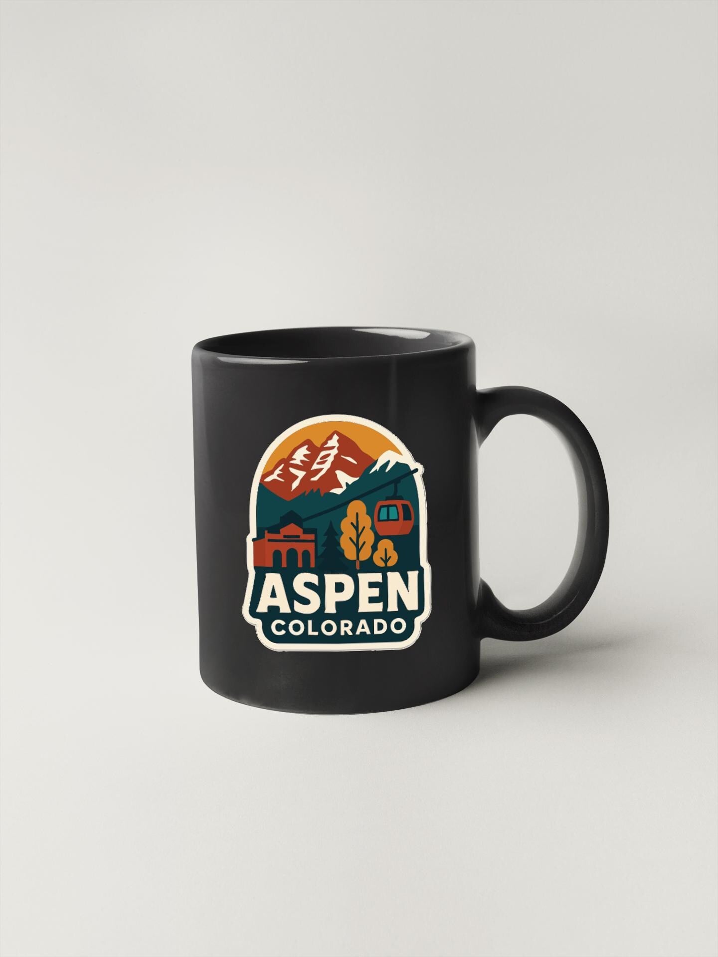 A black coffee mug with a colorful graphic design featuring mountains, buildings, and text that says "Aspen, Colorado".