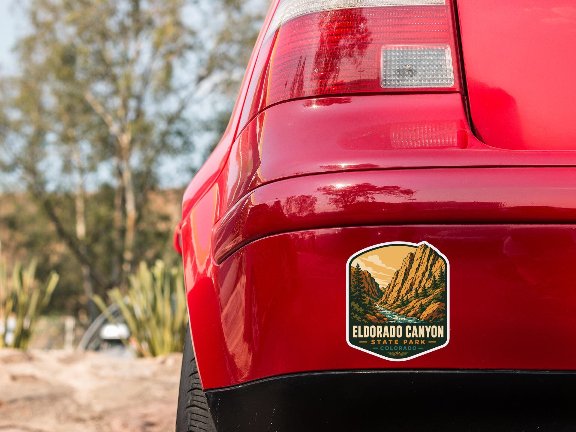 the rear end of a red car with a sticker on the back, featuring a scenic mountain landscape.