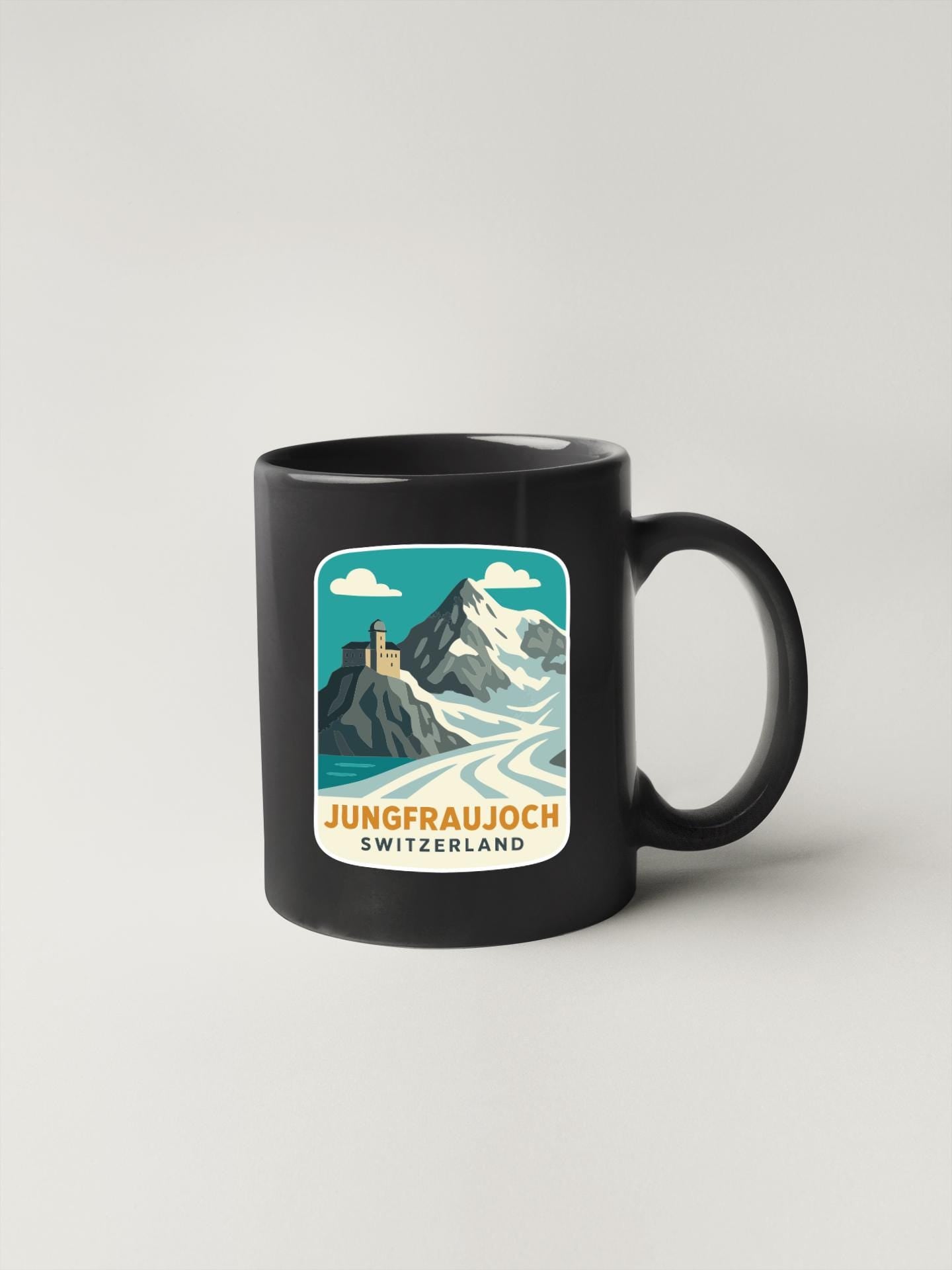 A black coffee mug with a graphic design depicting a mountain landscape and a castle, along with the text "Jungfraujoch SWITZERLAND".