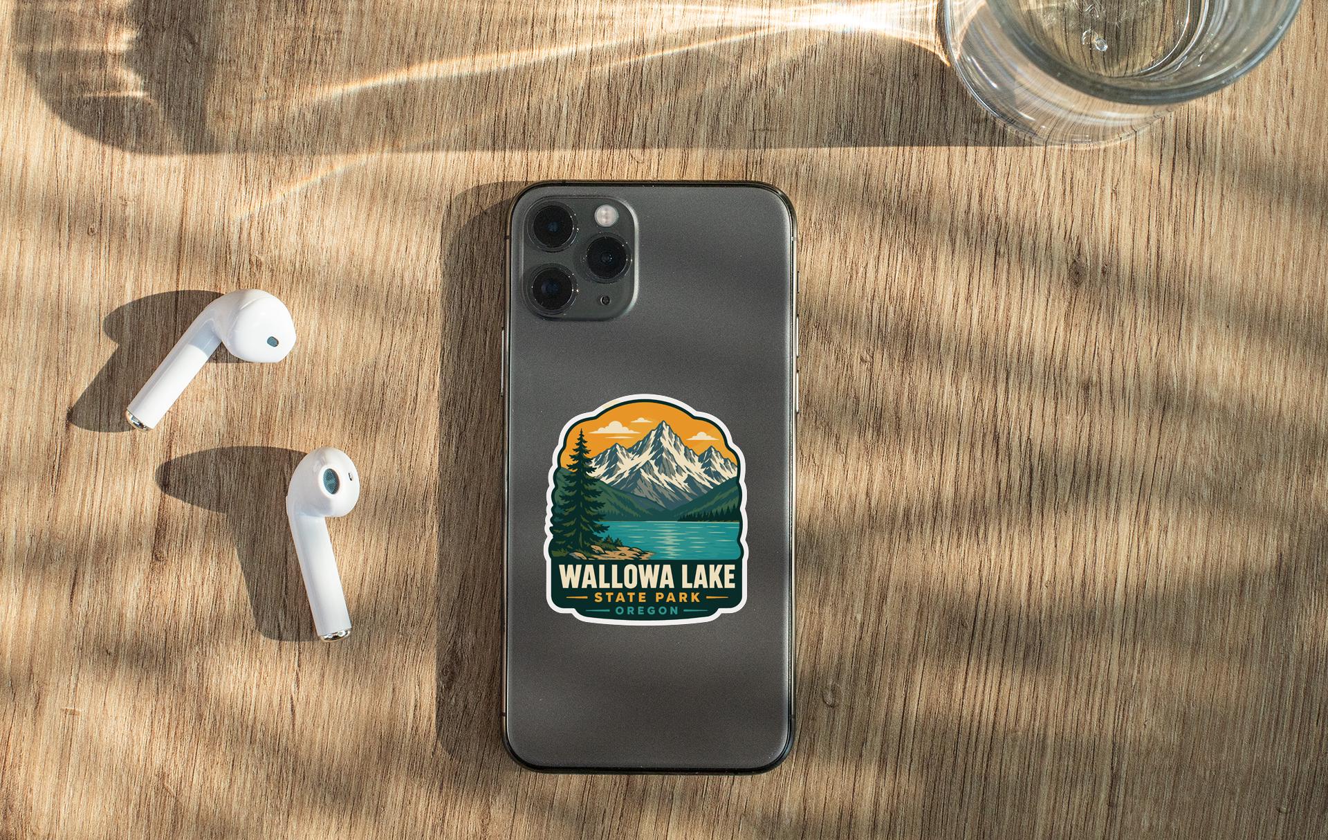a smartphone with a sticker on the back, placed on a wooden surface alongside a pair of white earbuds and a glass of water.