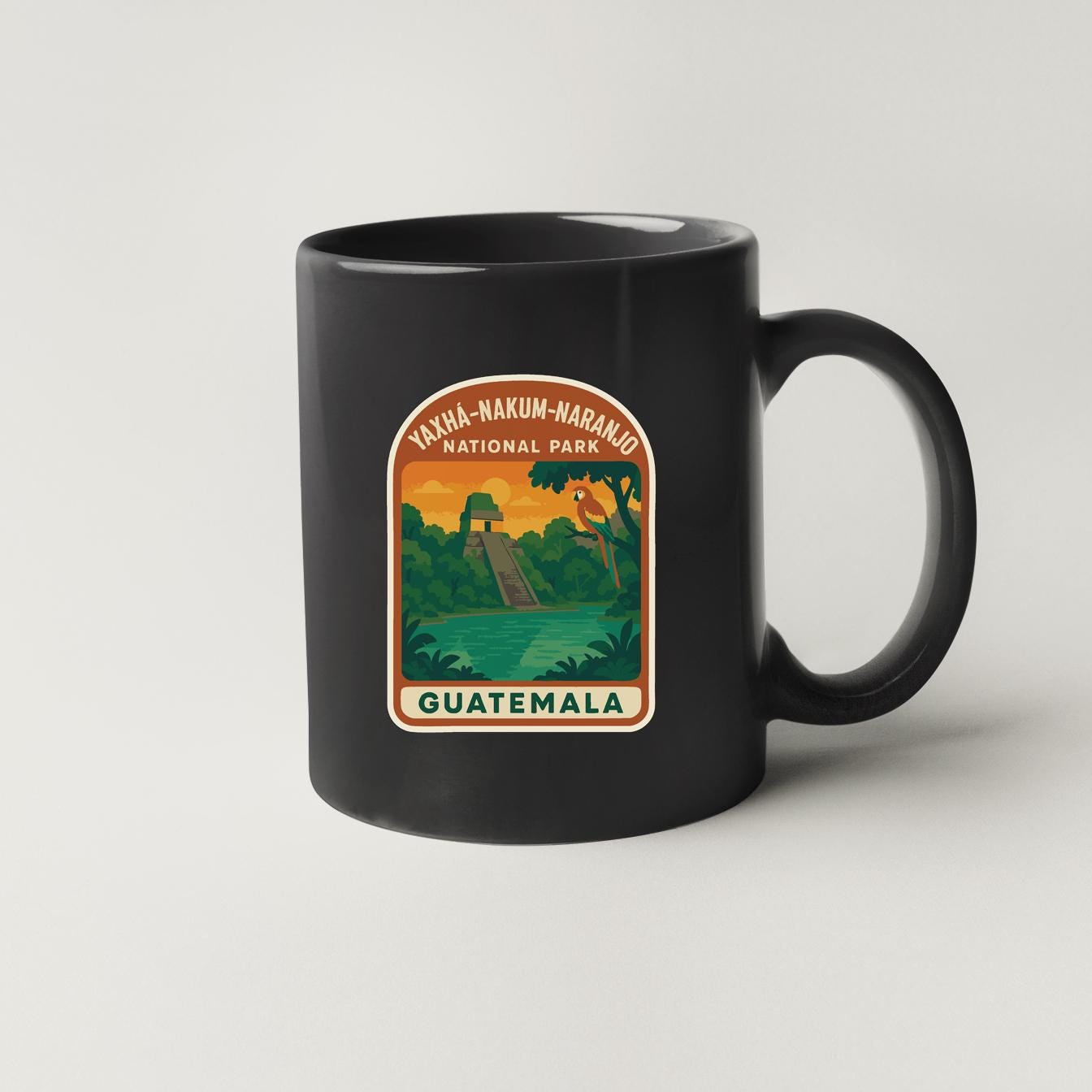 A black coffee mug with a graphic design depicting a tropical landscape, including a waterfall, palm trees, and a bird.