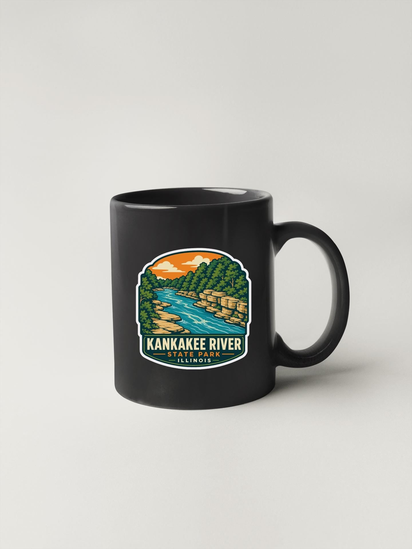 A black coffee mug with a colorful illustration of the Kankakee River and surrounding landscape.