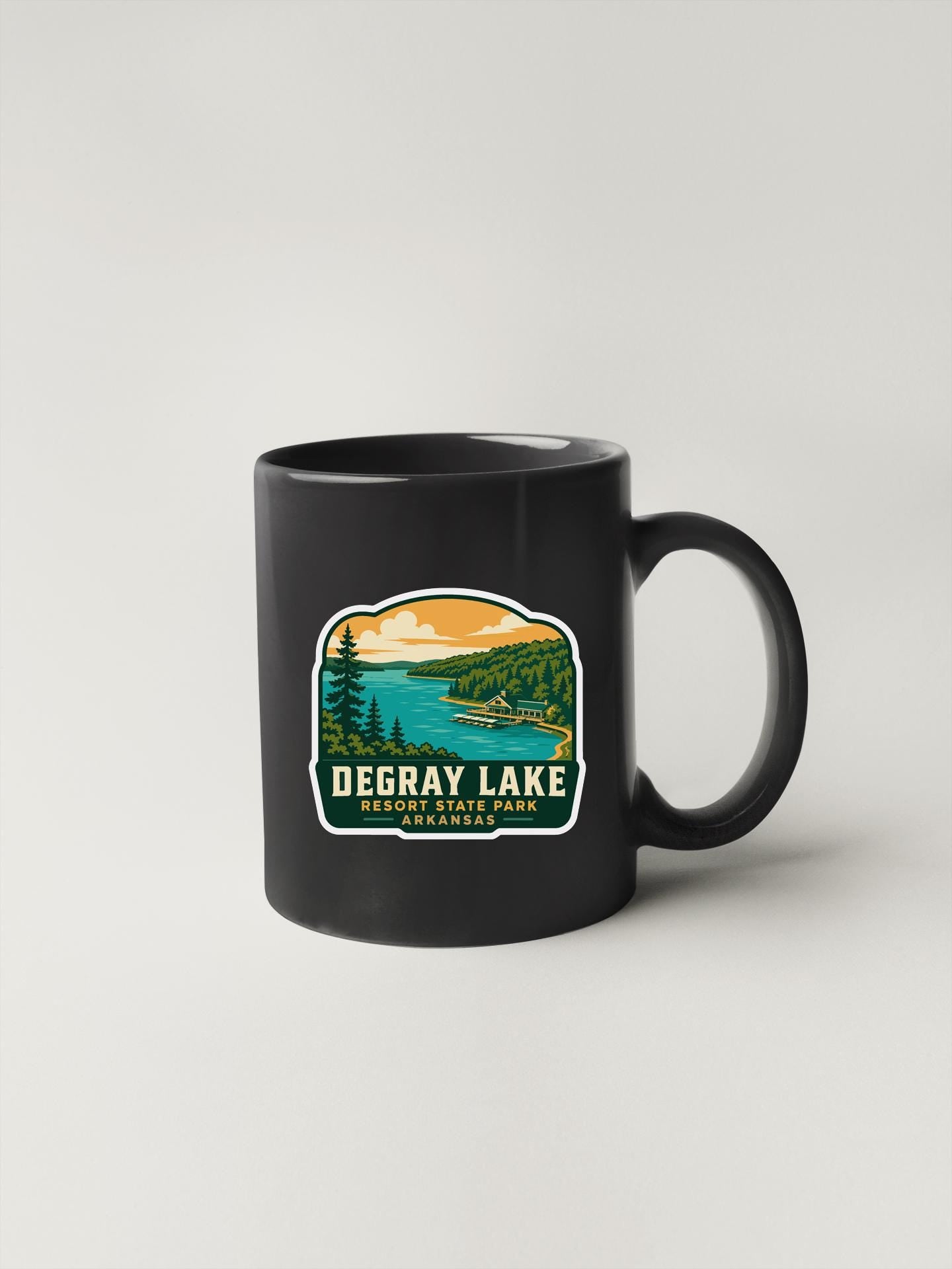 A black coffee mug with a sticker depicting a scenic landscape featuring a lake, mountains, and trees.