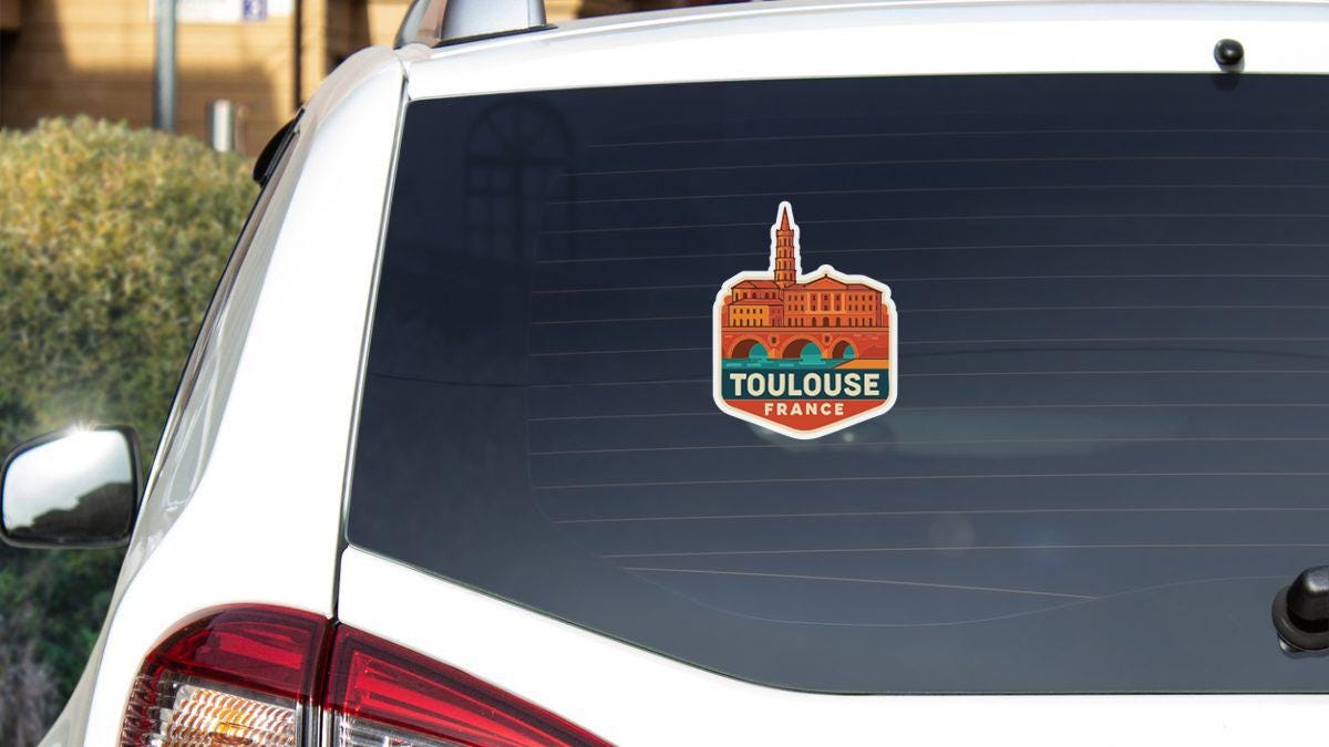A sticker on the rear window of a white car, depicting the Toulouse, France landmark.