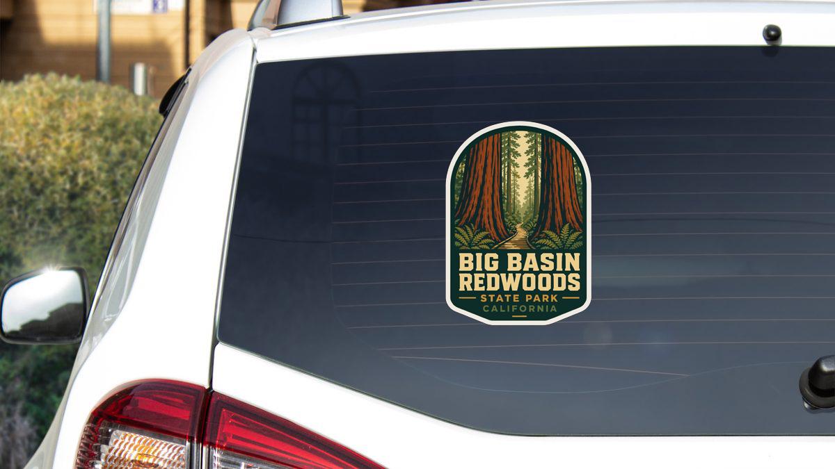A sticker on the rear window of a white car, featuring an illustration of a forest with tall trees and a path leading through it, along with the text "BIG BASIN REDWOODS STATE PARK CALIFORNIA".