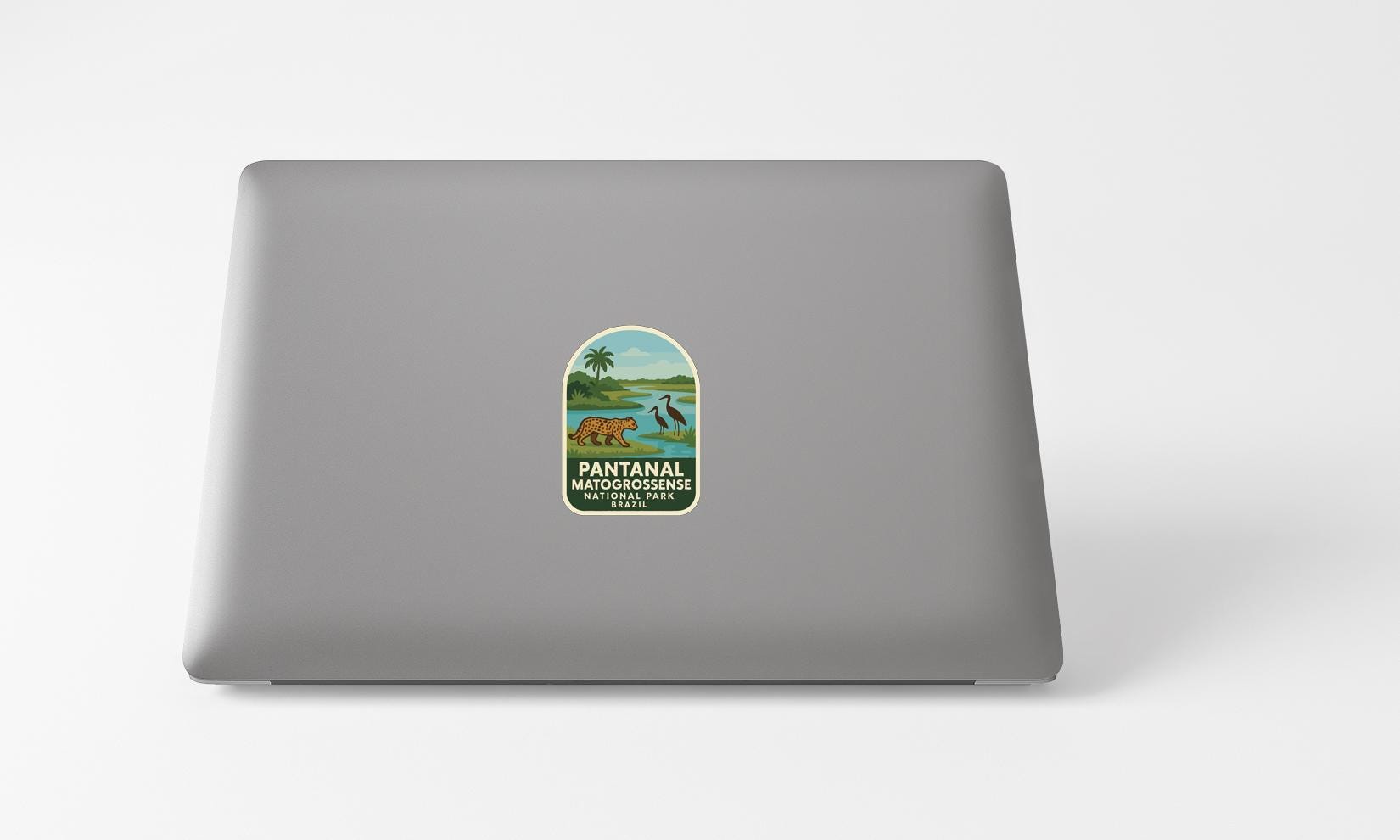 A sticker with a graphic of a bear and a tropical landscape, along with the text "PANTANAL MATOCROSSENISE NATURAL PARK, MEXICO" printed on a grey laptop.