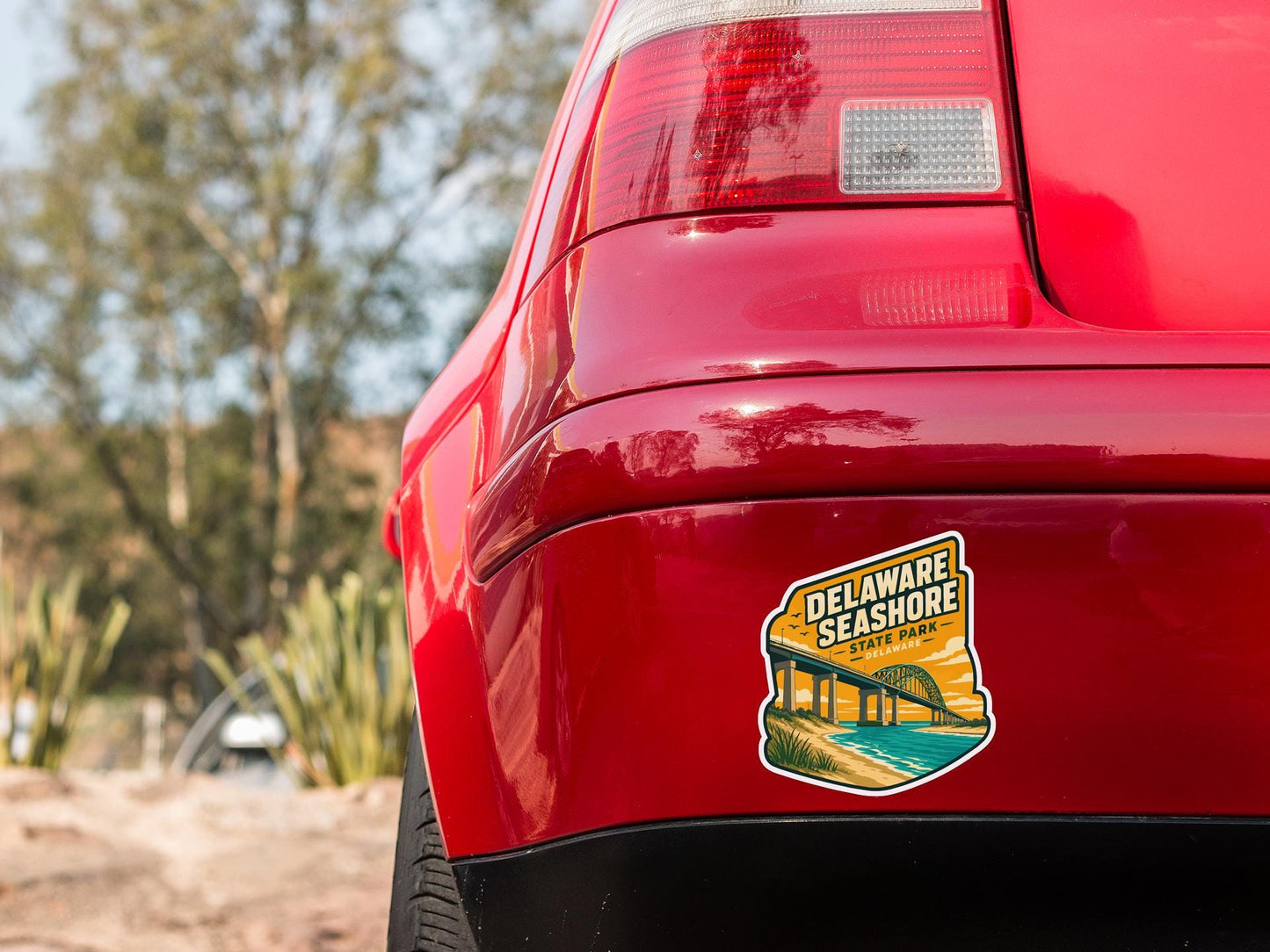 the rear end of a red car with a sticker on the bumper that says "Delaware Shore State Park".