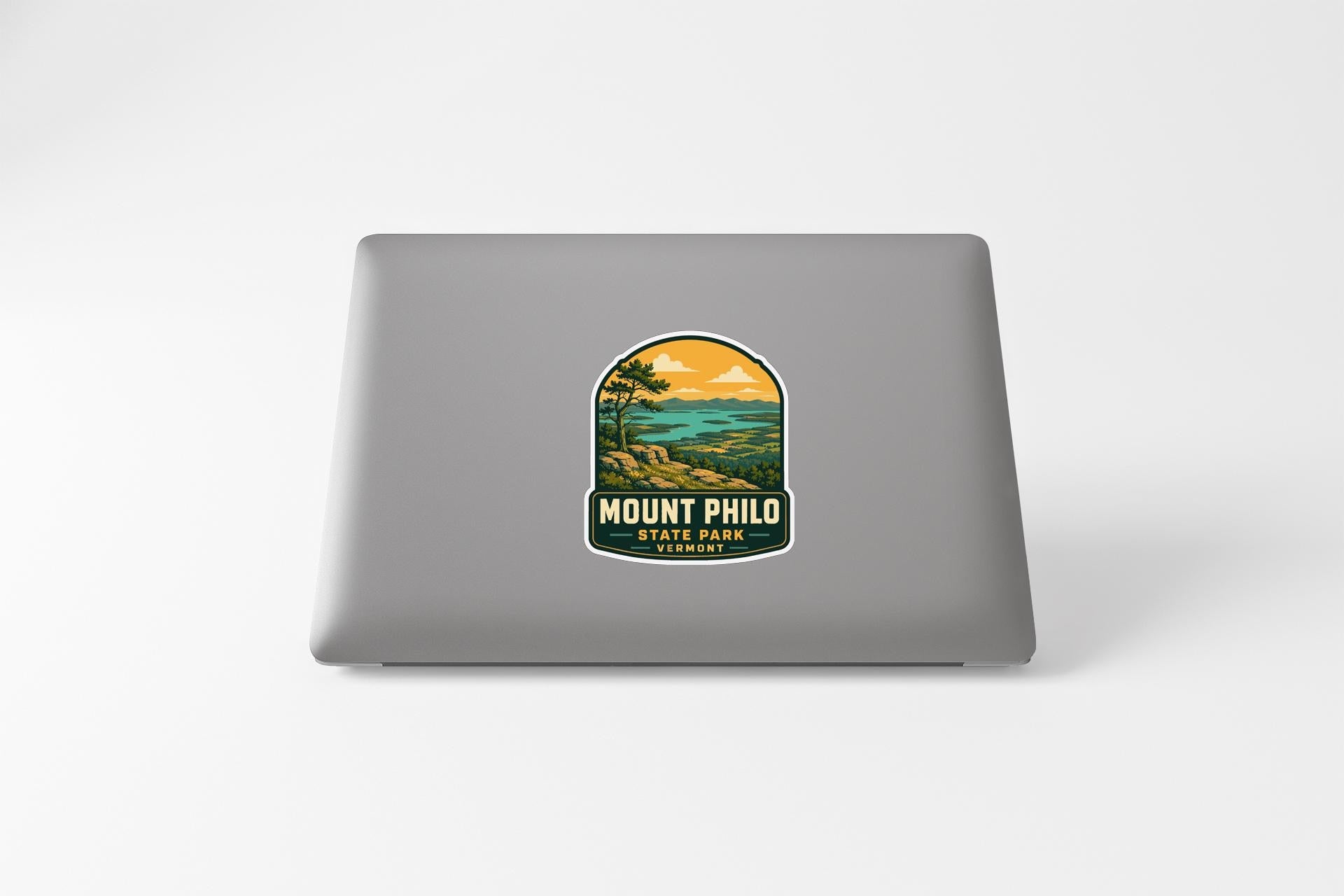 A sticker on the back of a laptop, depicting a scenic landscape with mountains, trees, and a body of water.