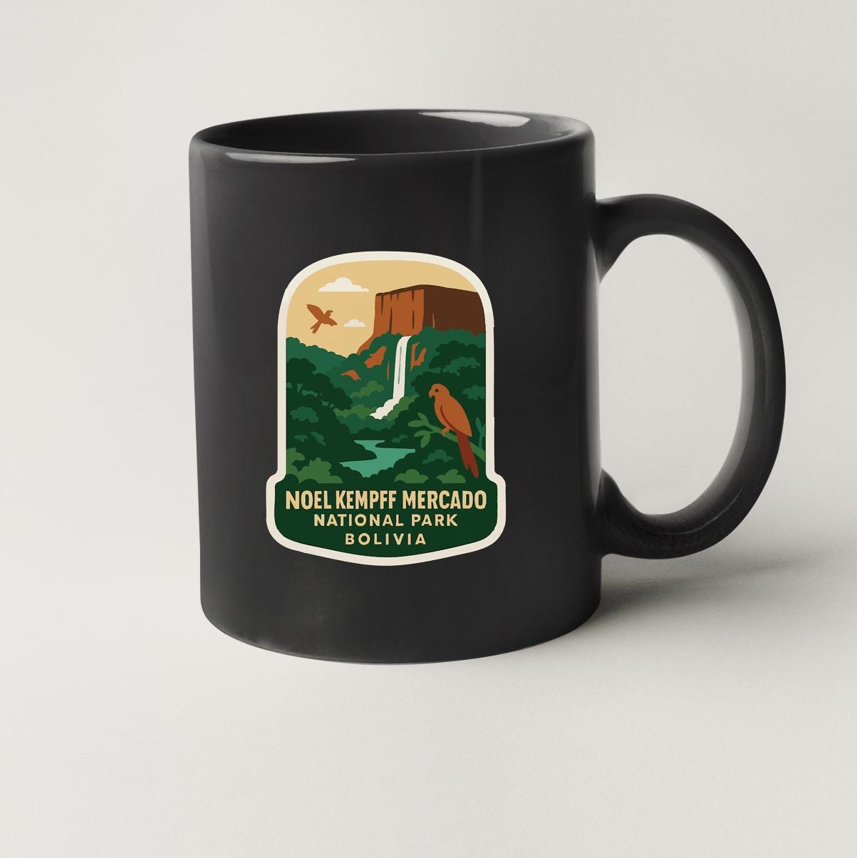 A black coffee mug with a sticker depicting a waterfall, birds, and a mountain in the background, along with the text "Noel Kempff Mercado National Park Bolivia".