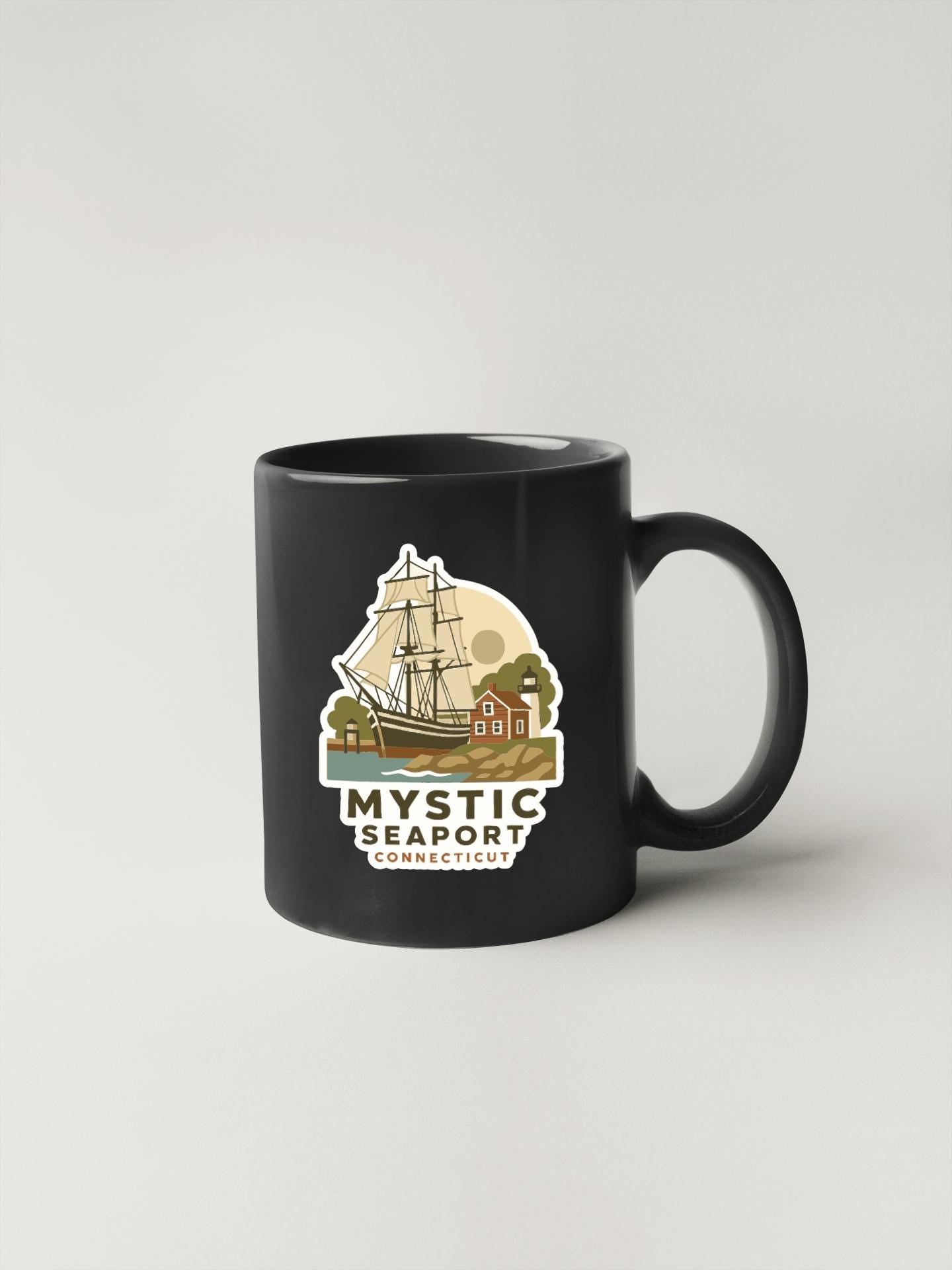 A black coffee mug with a graphic design depicting a sailing ship and a lighthouse, along with the text "MYSTIC SEAPORT CONNECTICUT".