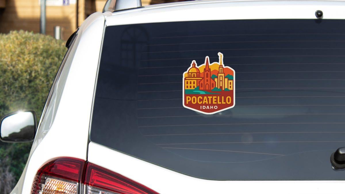 A sticker on the rear window of a white car, featuring an illustration of a city skyline with buildings and a church.