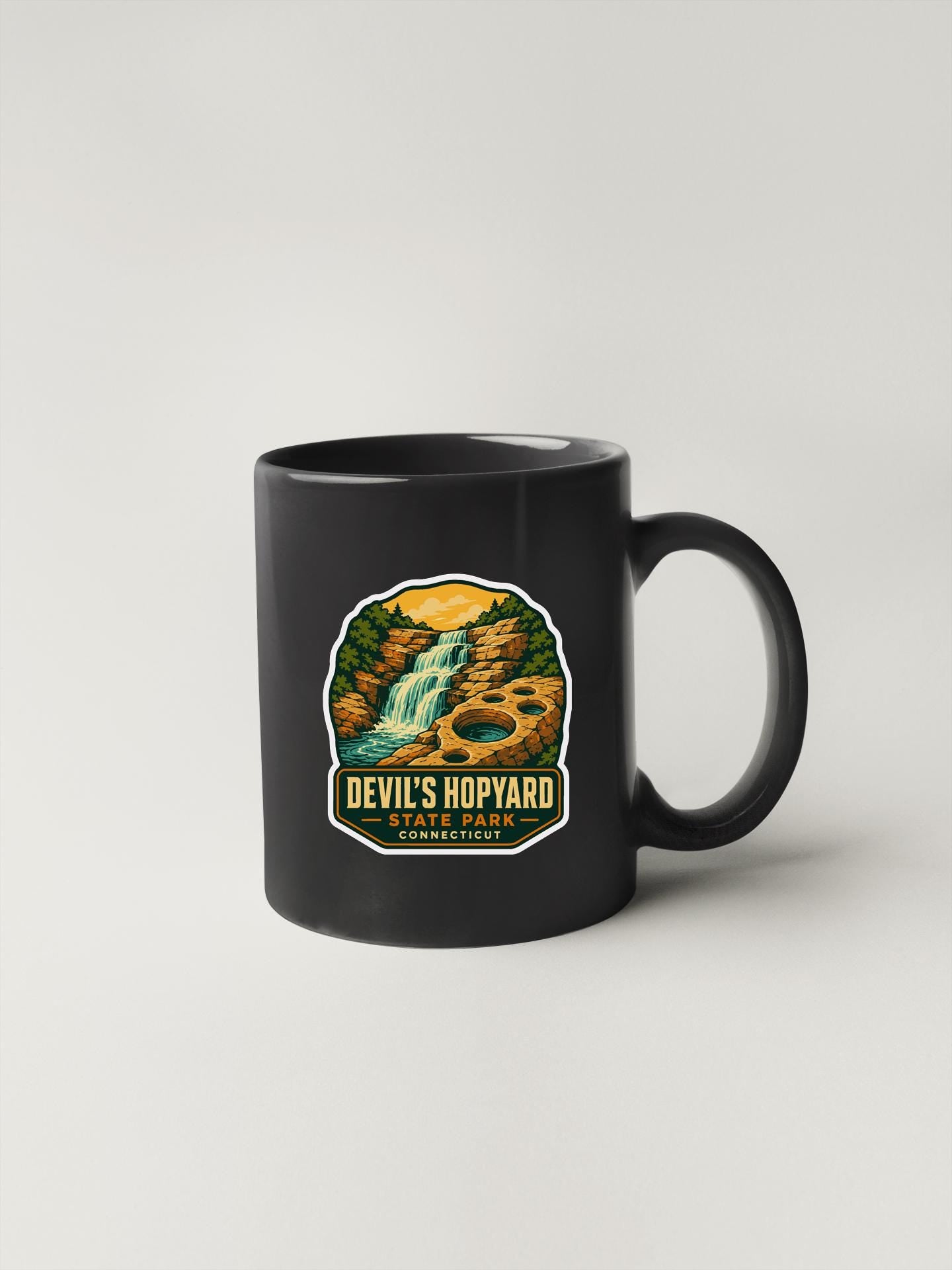A black coffee mug with a graphic design depicting a waterfall and forest.