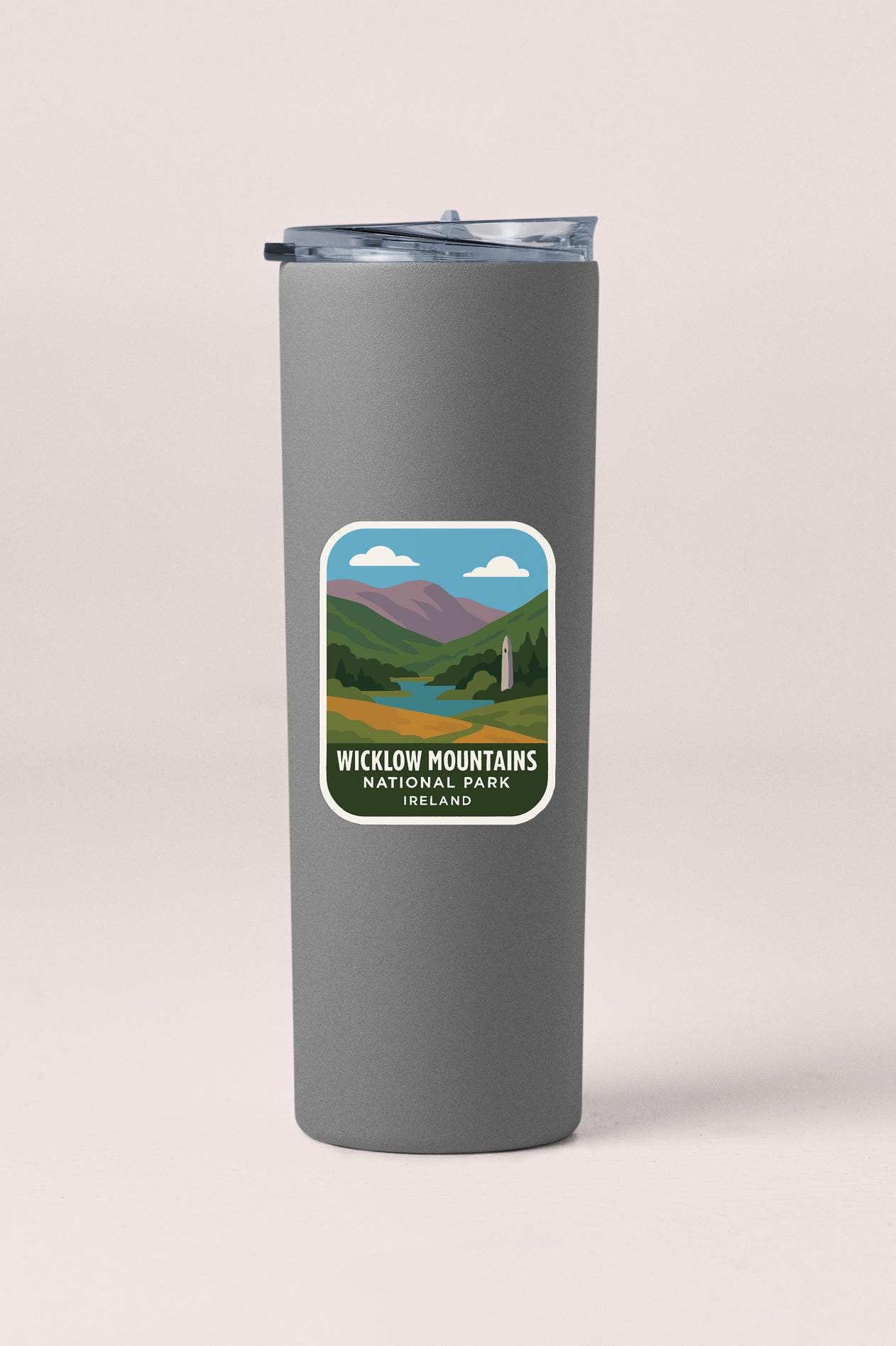 A gray insulated tumbler with a label that features a scenic mountain landscape.