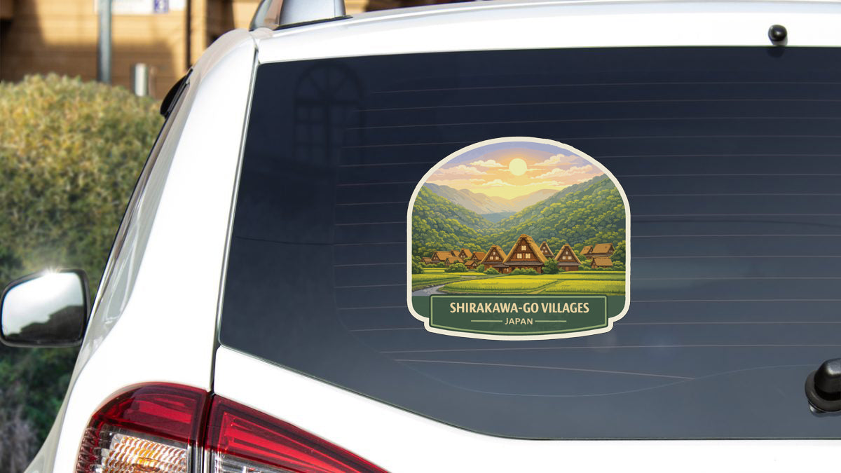 A sticker on the rear window of a car depicting a scenic landscape with traditional Japanese houses and mountains in the background.