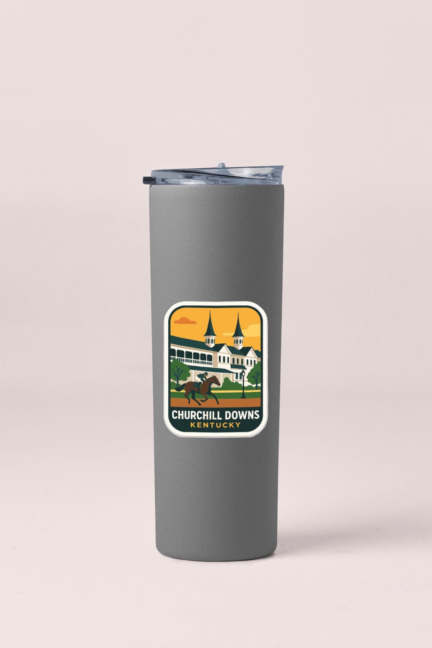 A gray insulated tumbler with a sticker depicting a horse and jockey racing at the Churchill Downs Kentucky racetrack.