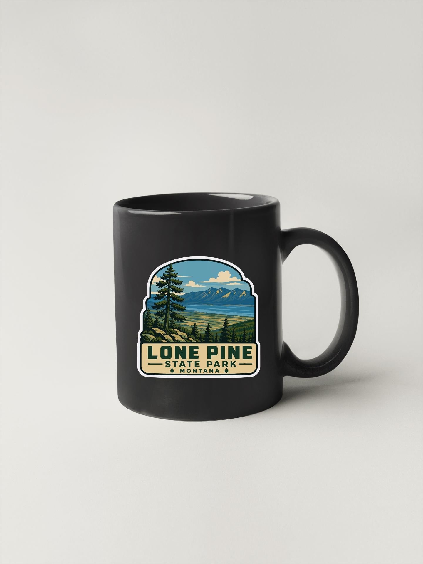 A black coffee mug with a graphic design depicting a scenic landscape, including mountains, trees, and a body of water.