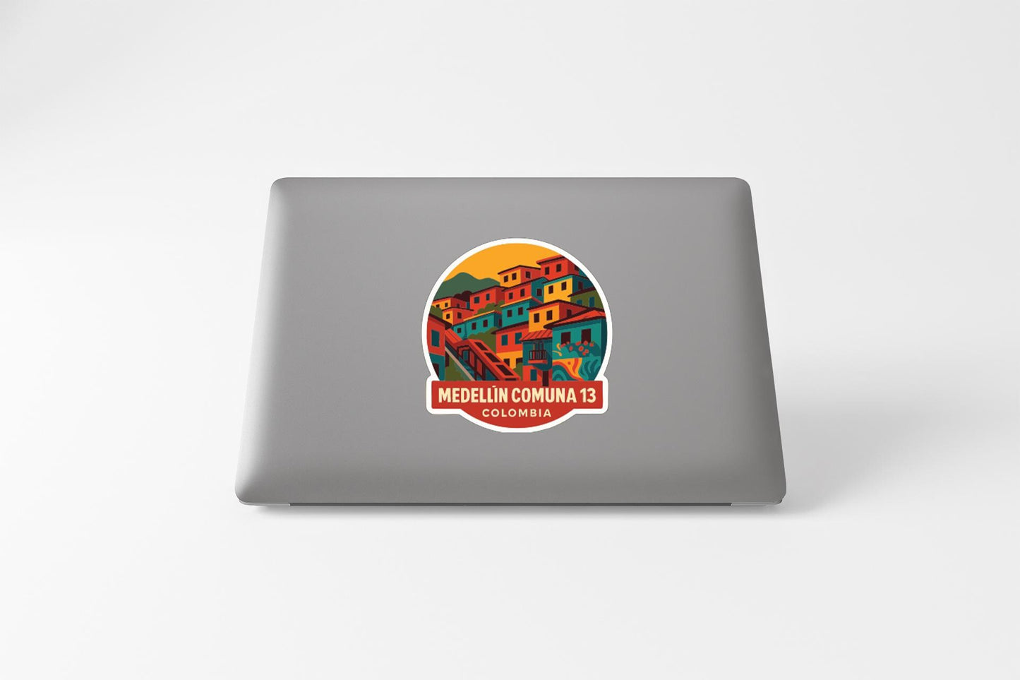 a sticker with a colorful illustration of a town or village, along with the text "MEDELLÍN COMUNA 13 COLOMBIA".