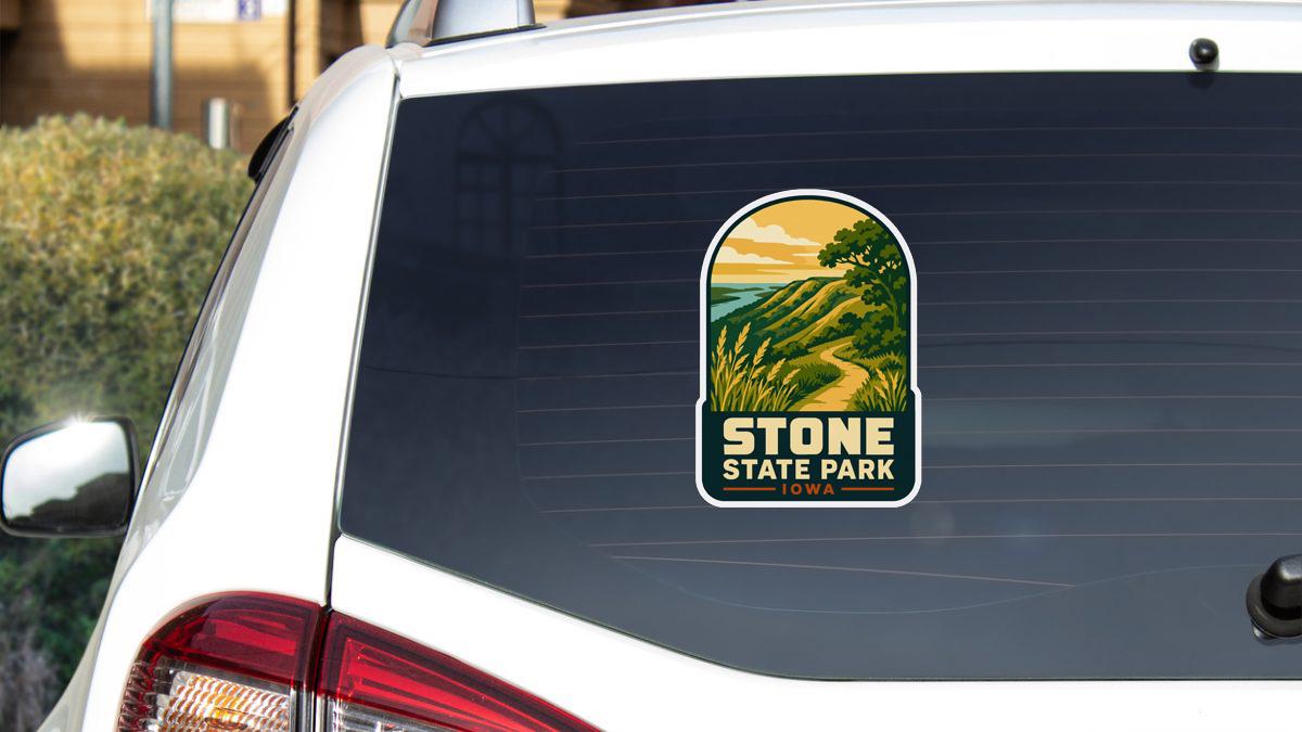 A sticker on the rear window of a white car, depicting a scenic landscape with a winding road and a mountain in the background.
