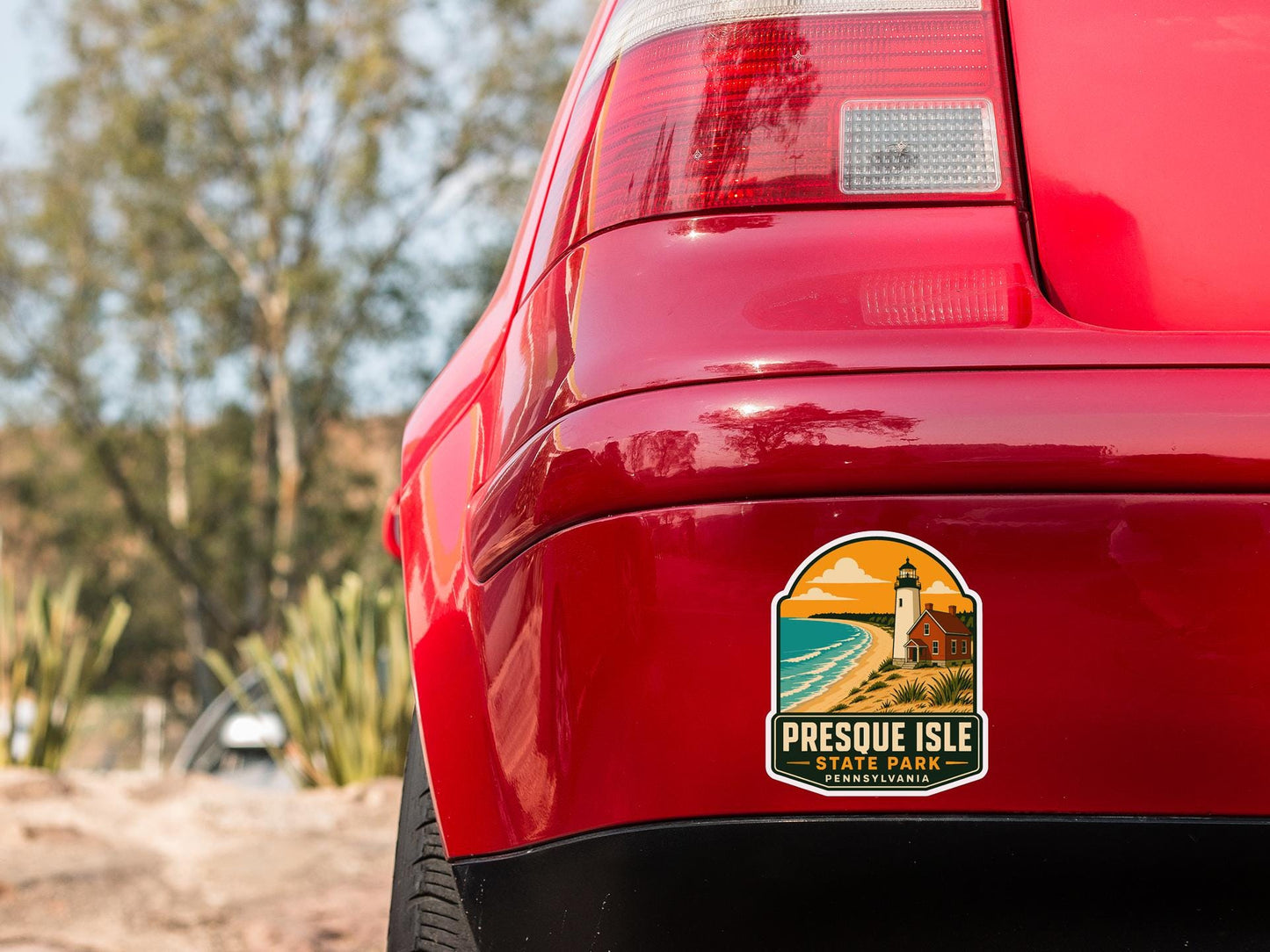 the rear end of a red car with a sticker on the back window that says "Presque Isle State Park, Pennsylvania".