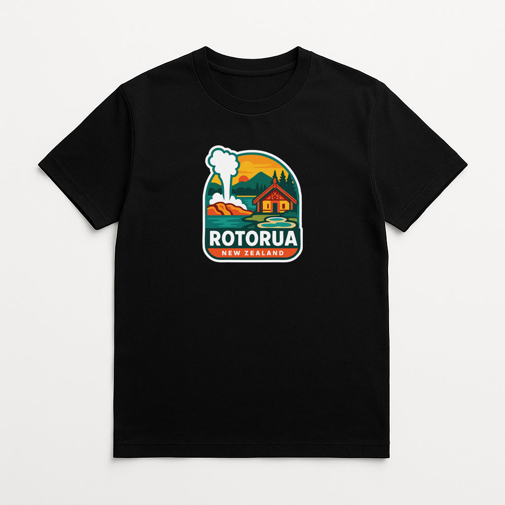 A black t-shirt with a graphic design depicting a scenic landscape with a house, mountains, and a steam tower, along with the text "ROTORUA NEW ZEALAND".