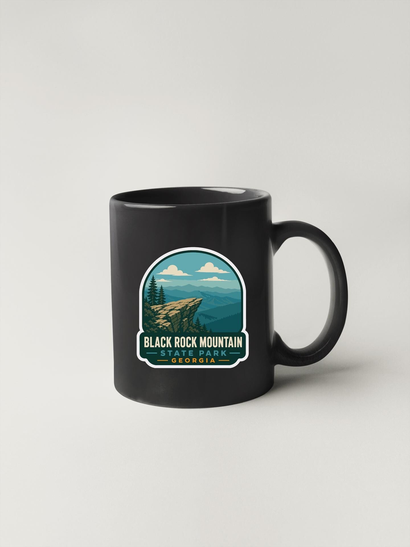 A black coffee mug with a graphic design depicting a scenic mountain landscape.