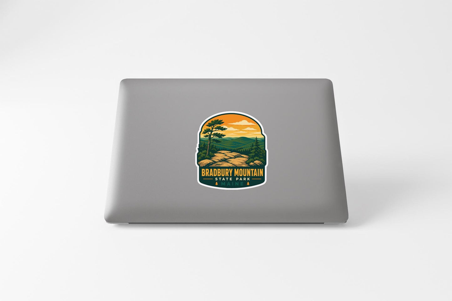 A sticker on the back of a laptop, depicting a scenic landscape with mountains, trees, and a sunset.