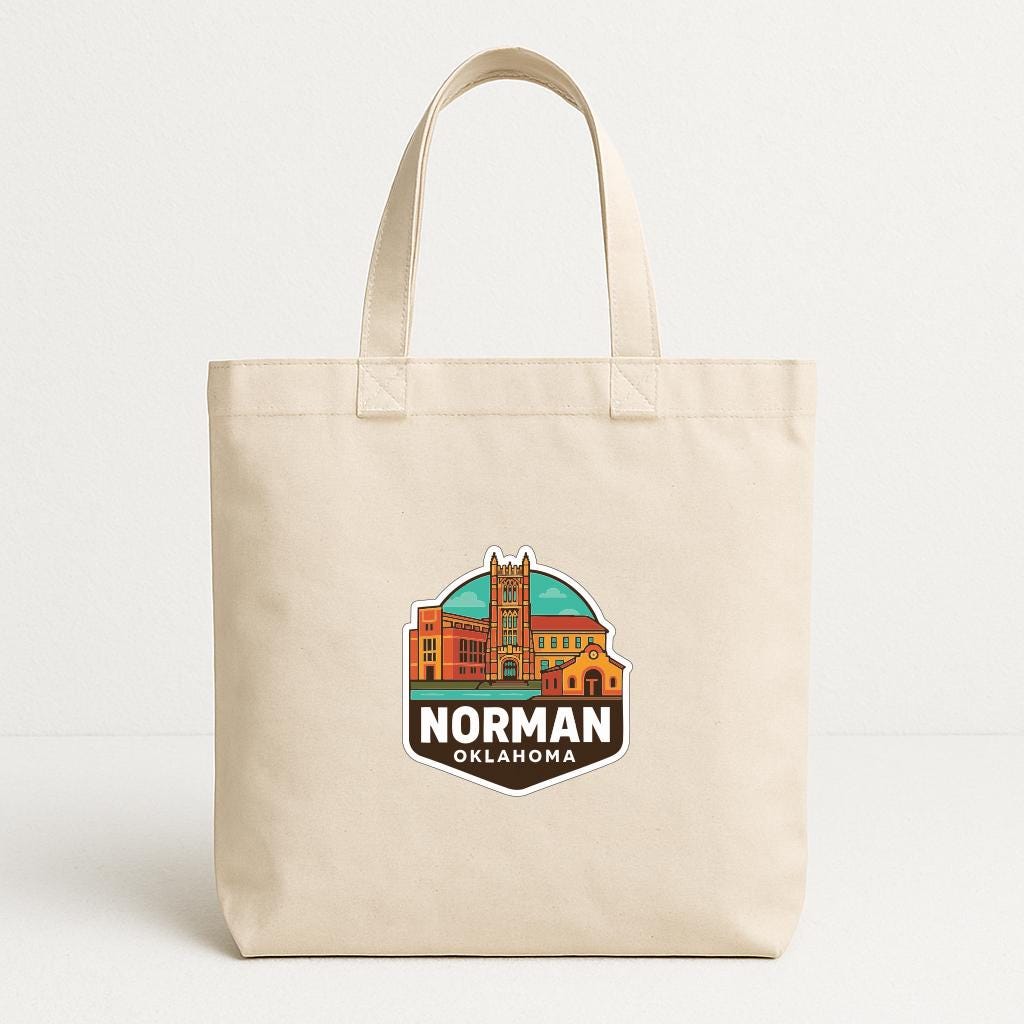 A beige tote bag with a graphic design featuring a city skyline and the text "NORMAN OKLAHOMA" printed on it.