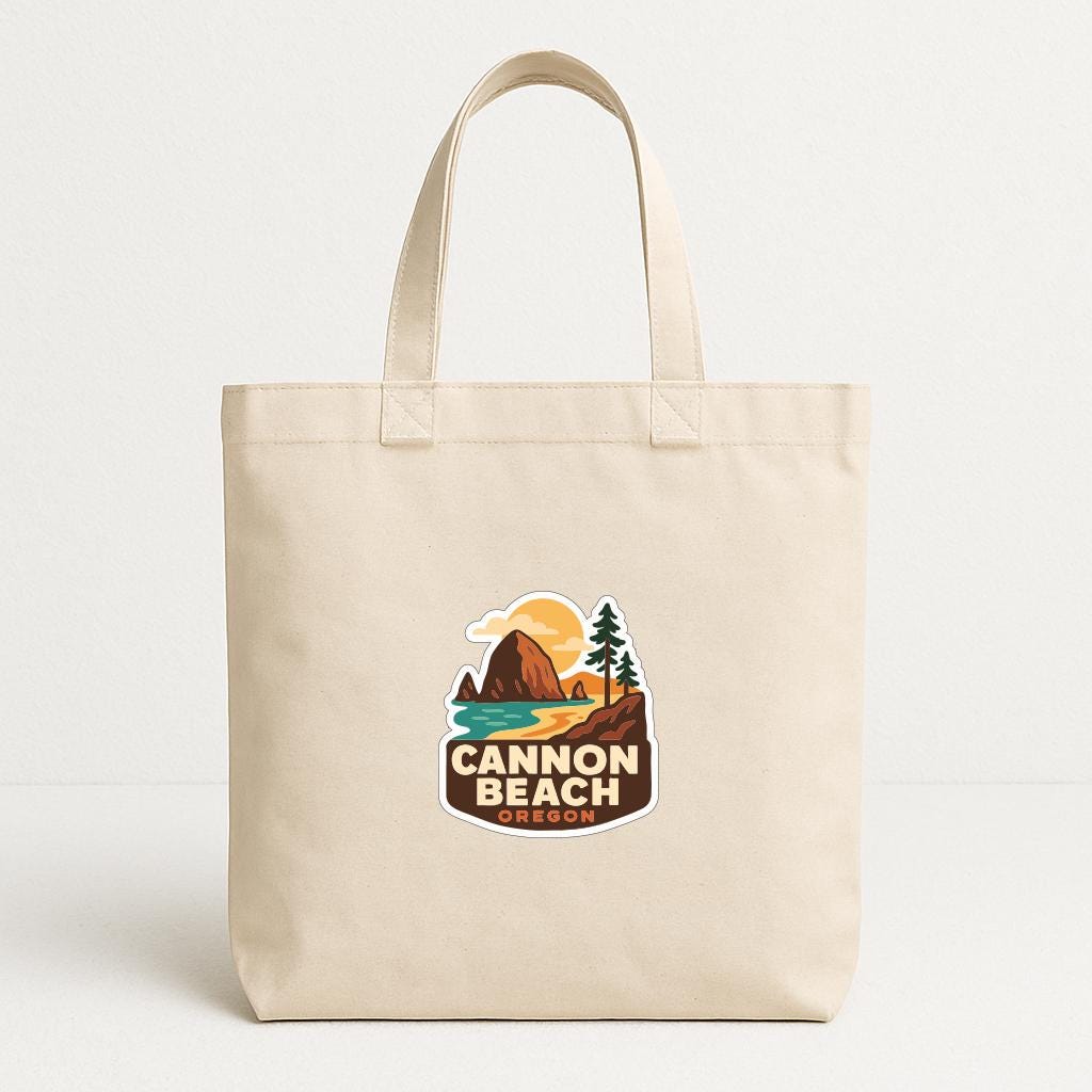 A beige tote bag with a printed logo that says "Cannon Beach Oregon".