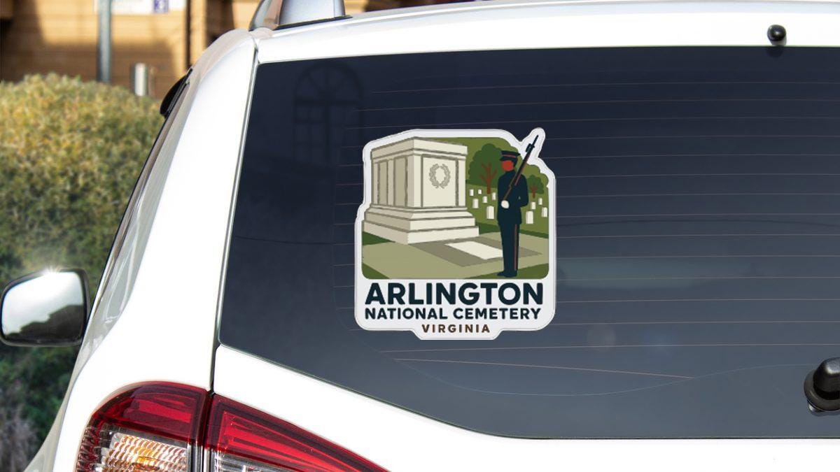 A sticker on the rear window of a white car, depicting a monument and a soldier, with the text "ARLINGTON NATIONAL CEMETERY VIRGINIA".