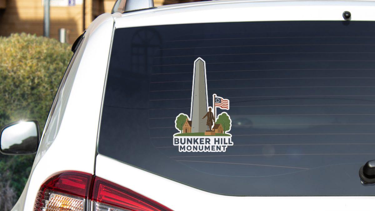 A sticker on the rear window of a white car depicting the Bunker Hill Monument, an American military base located in Boston, Massachusetts.