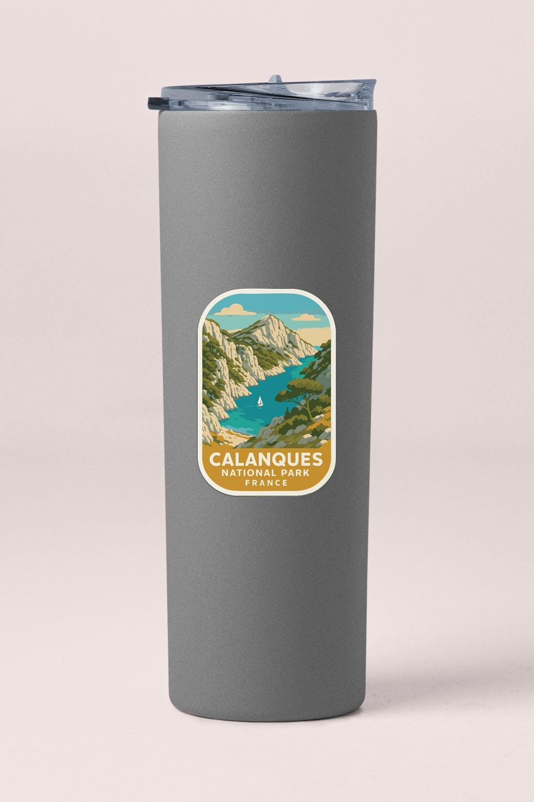 A gray insulated tumbler with a label that features a scenic mountain landscape and a sailboat on a lake.