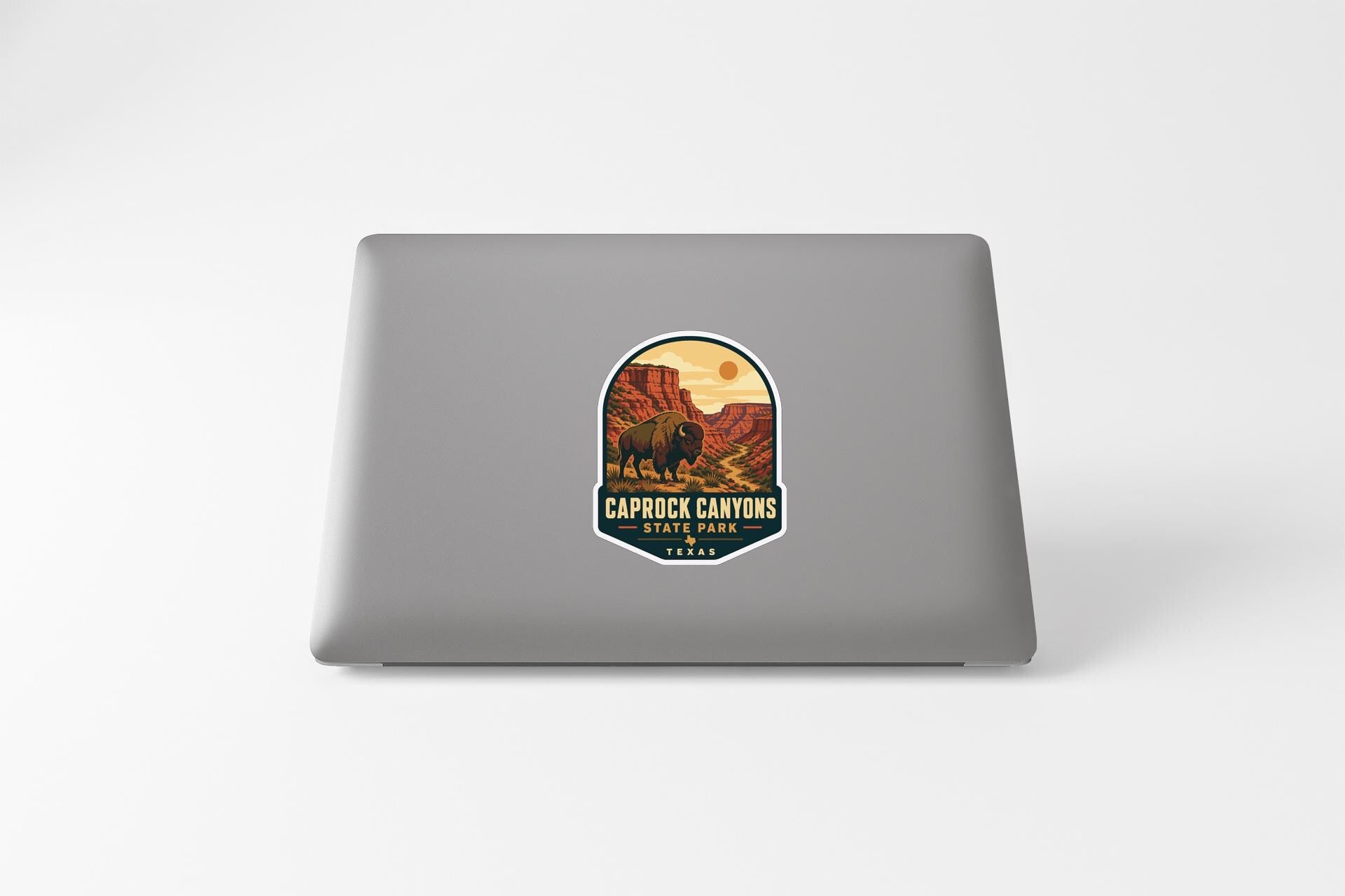 a sticker on a laptop that depicts a scenic landscape with a mountain range and a buffalo in the foreground.