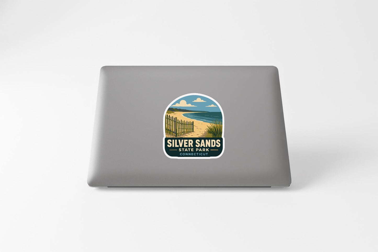 A sticker on the back of a laptop, depicting a beach scene with a path leading to the beach and a fence along the path.