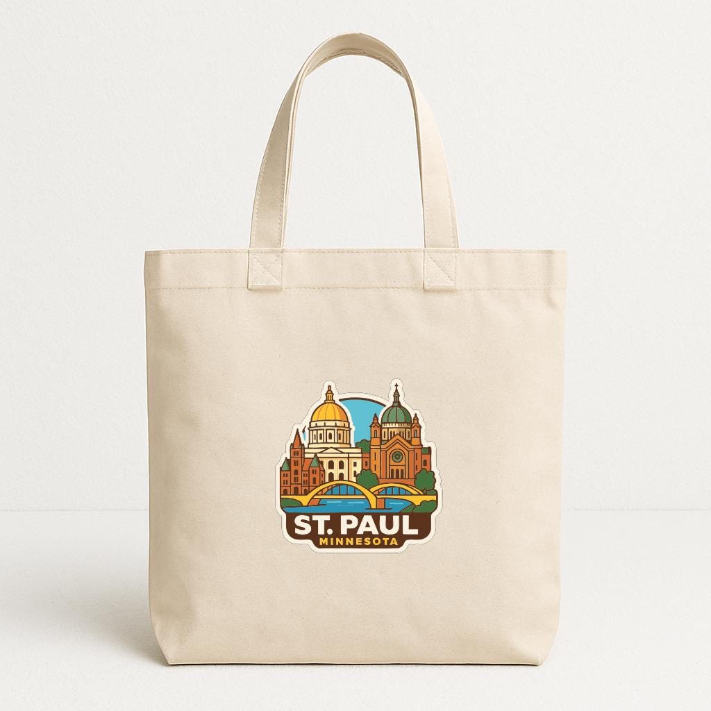 A beige tote bag with a printed design of St. Paul, Minnesota, featuring a cityscape with domes and a bridge.