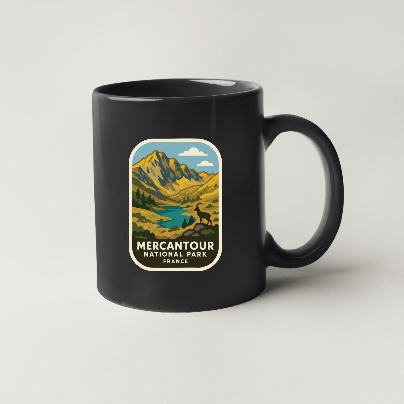 A black coffee mug with a graphic design depicting a mountain landscape and a river, along with the text "MERCANTOUR NATIONAL PARK FRANCE".