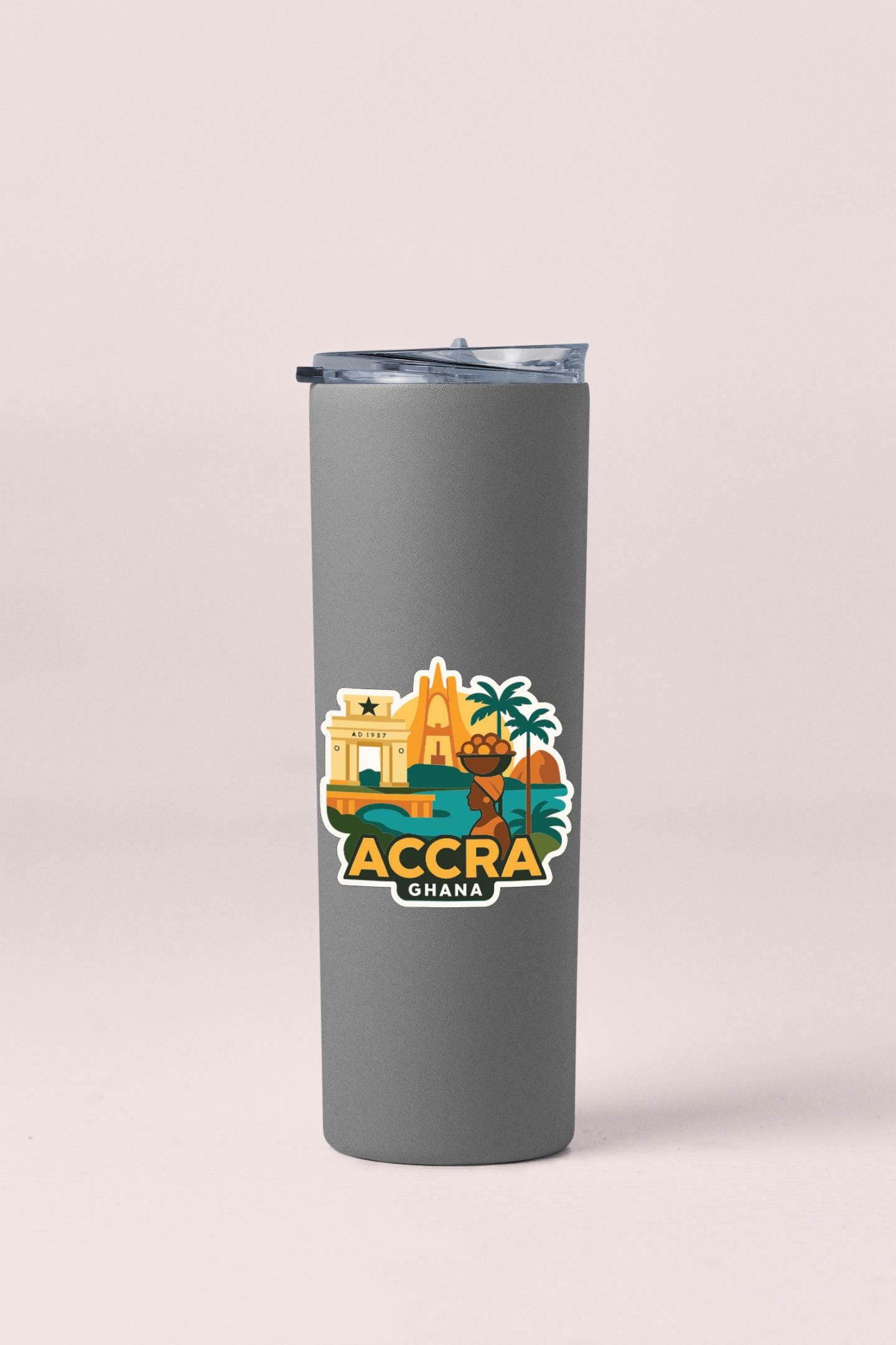 A gray insulated tumbler with a colorful sticker depicting Accra, Ghana, featuring a building, palm trees, and other landmarks.
