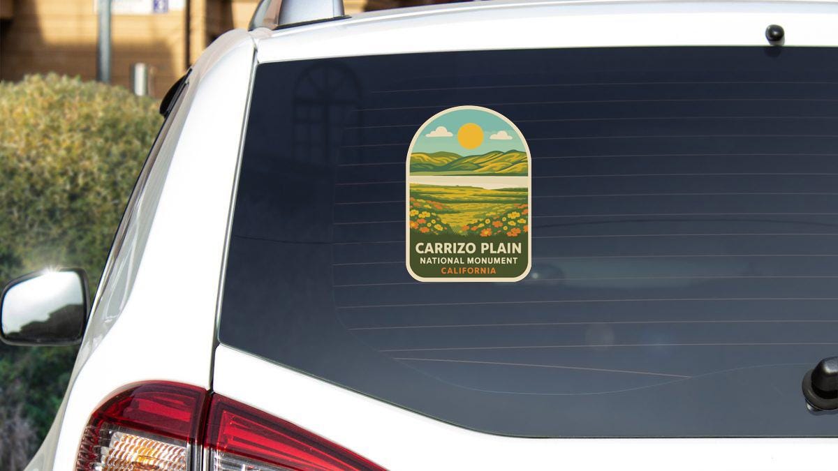 the rear window of a white car with a sticker on it, depicting a scenic landscape with mountains and a sun.