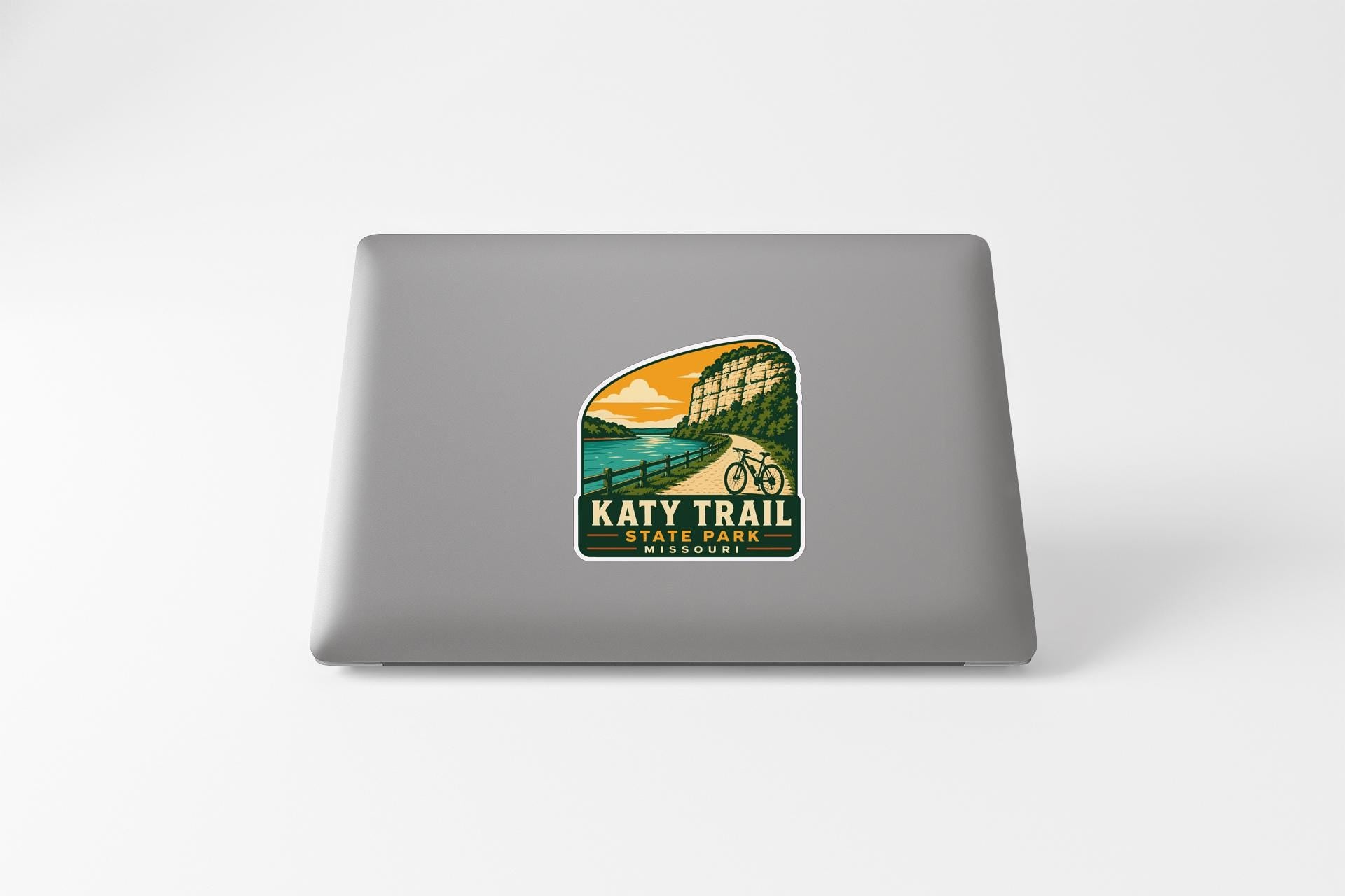 A sticker on the back of a laptop that features a scenic landscape with a mountain, a river, and a bicycle.