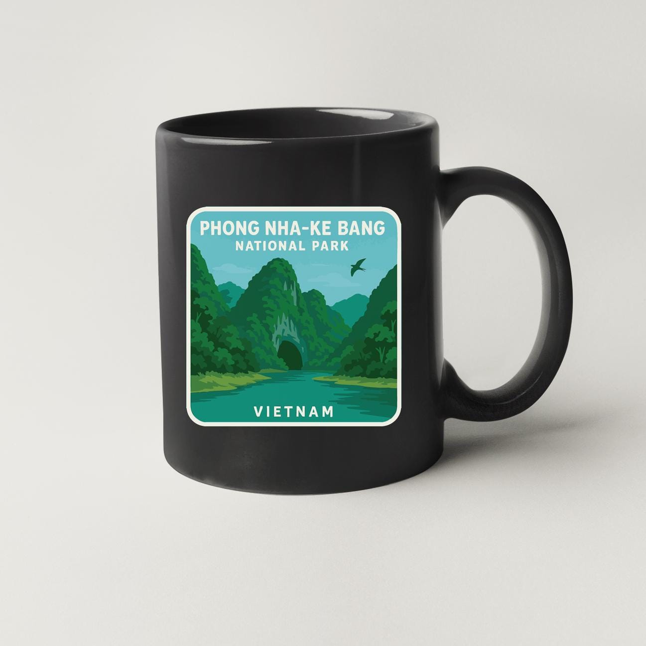 A black coffee mug with a graphic design depicting the Phong Nha-Ke Bang National Park in Vietnam, featuring a river, mountains, and a bird in flight.