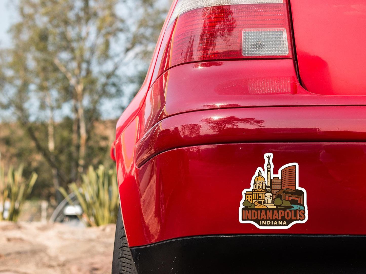 the rear end of a red car with a sticker on the trunk that features an illustration of a city skyline.