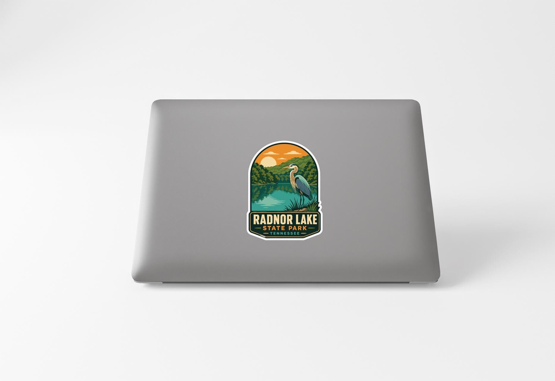 A sticker on the back of a laptop, depicting a scenic landscape with a lake, mountains, and a bird.
