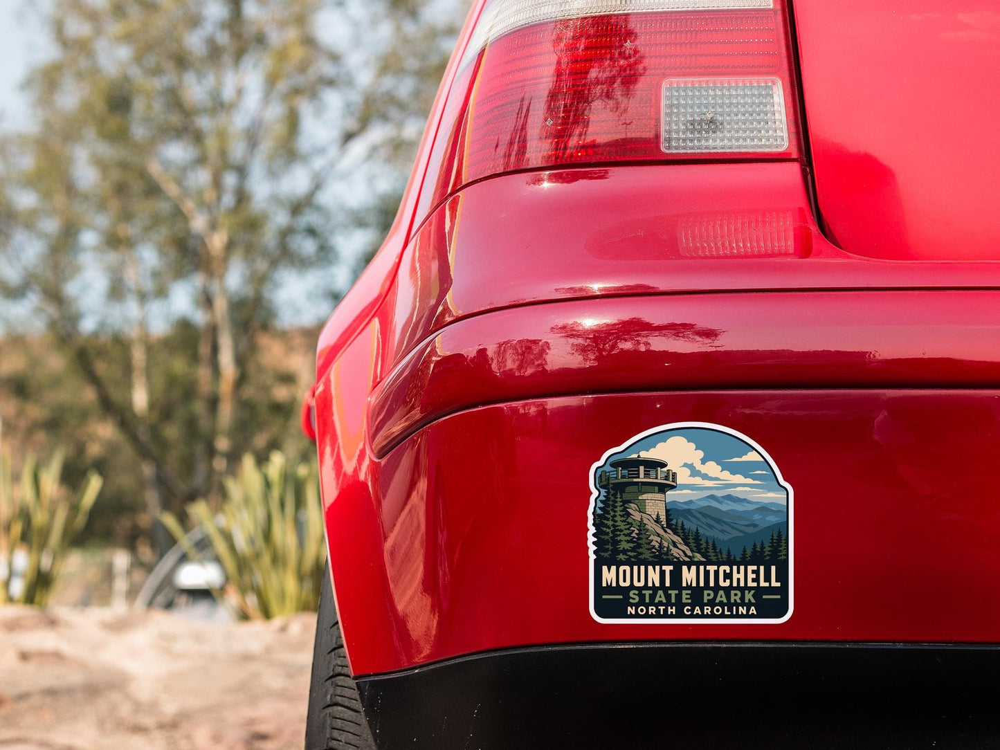 the rear end of a red car with a sticker on the trunk that says "Mount Mitchell State Park North Carolina".