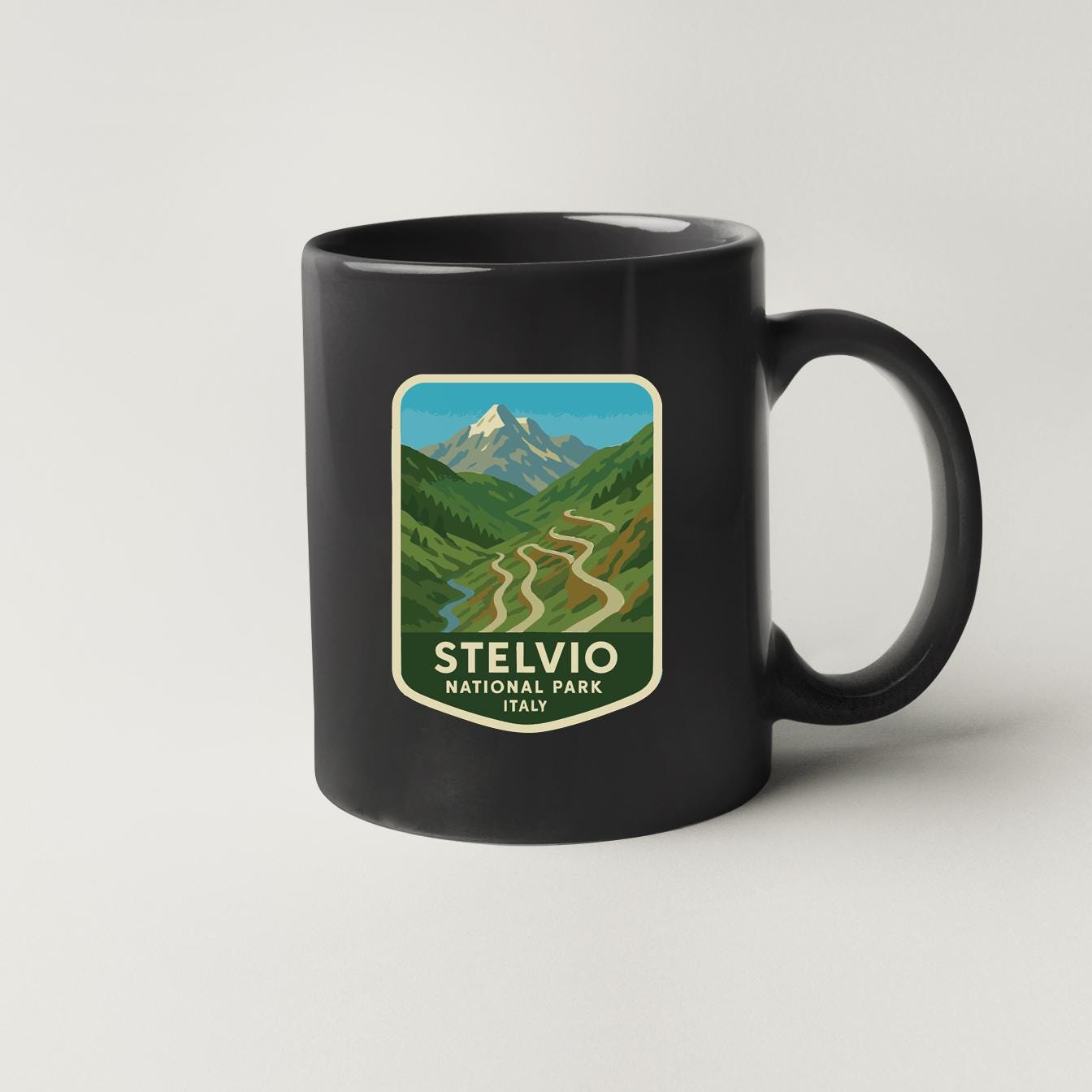 A black coffee mug with a graphic design depicting a mountain landscape and winding roads, along with the text "STELVIO NATIONAL PARK ITALY".