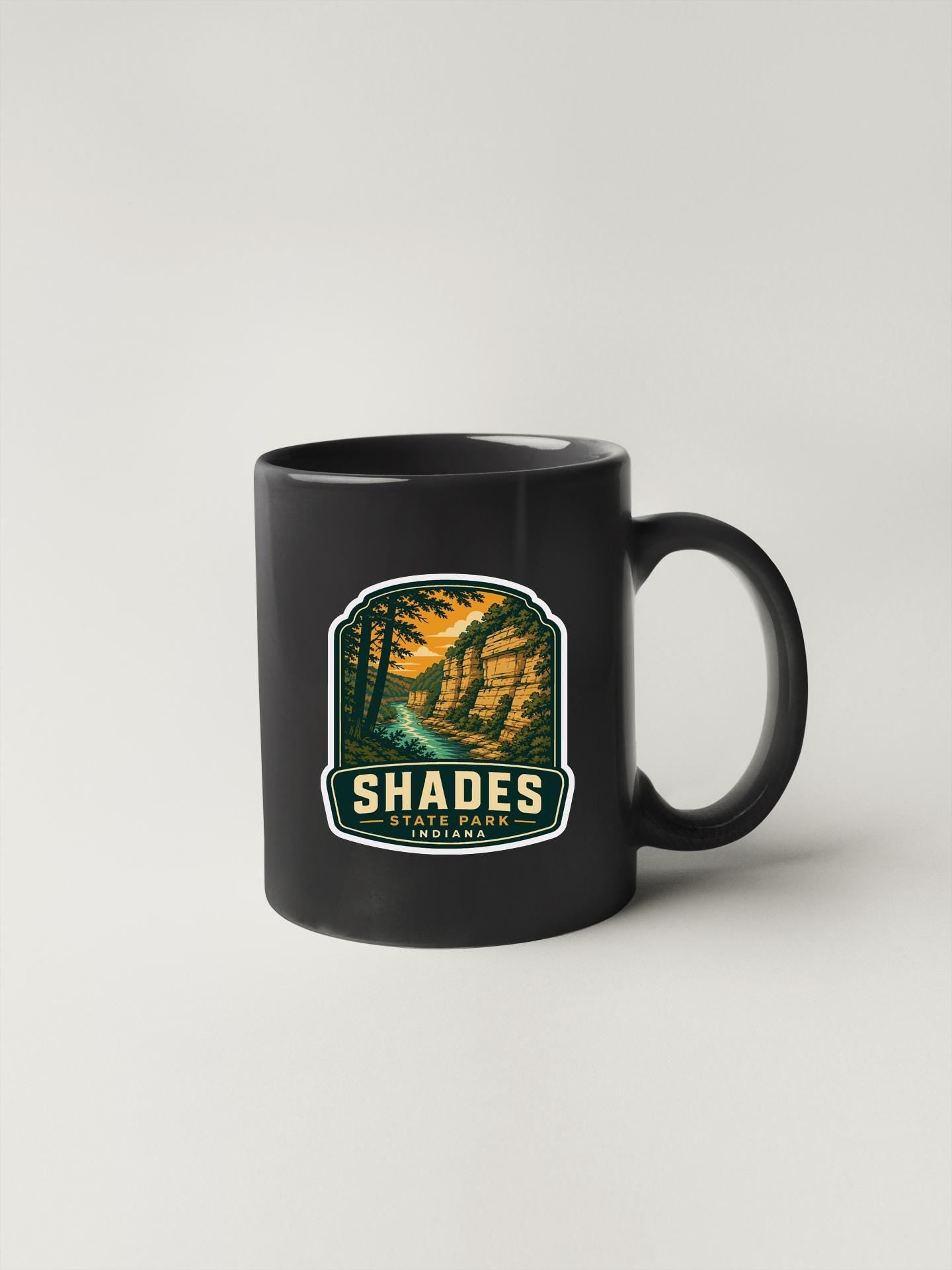 A black coffee mug with a graphic design depicting a scenic landscape, featuring a river and mountains.