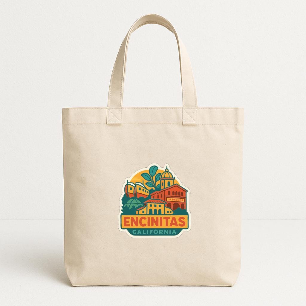 A beige tote bag with a colorful graphic of a building and the text "ENCINITAS CALIFORNIA" printed on it.