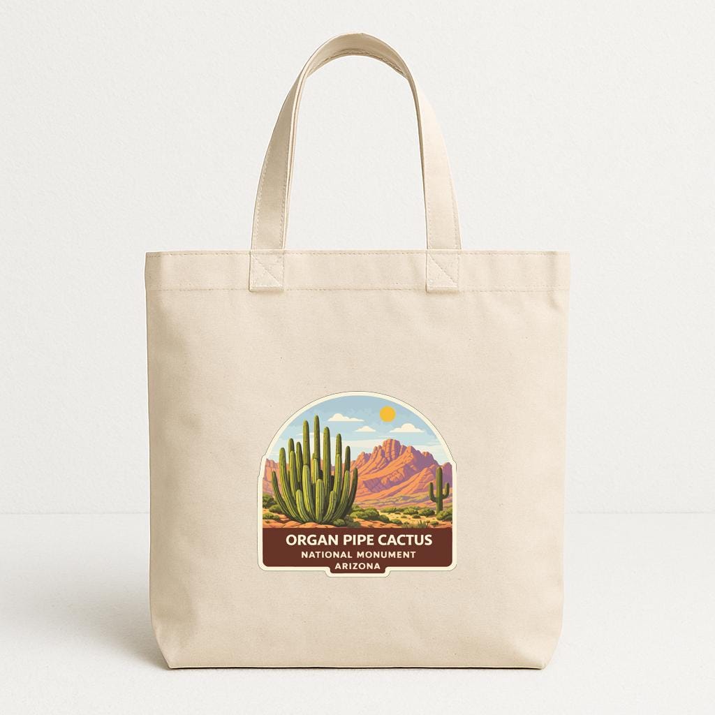 A beige tote bag with a label that says "ORGAN PIPE CACTUS NATIONAL MOUNTAIN ARIZONA" and features an illustration of a cactus and mountains.